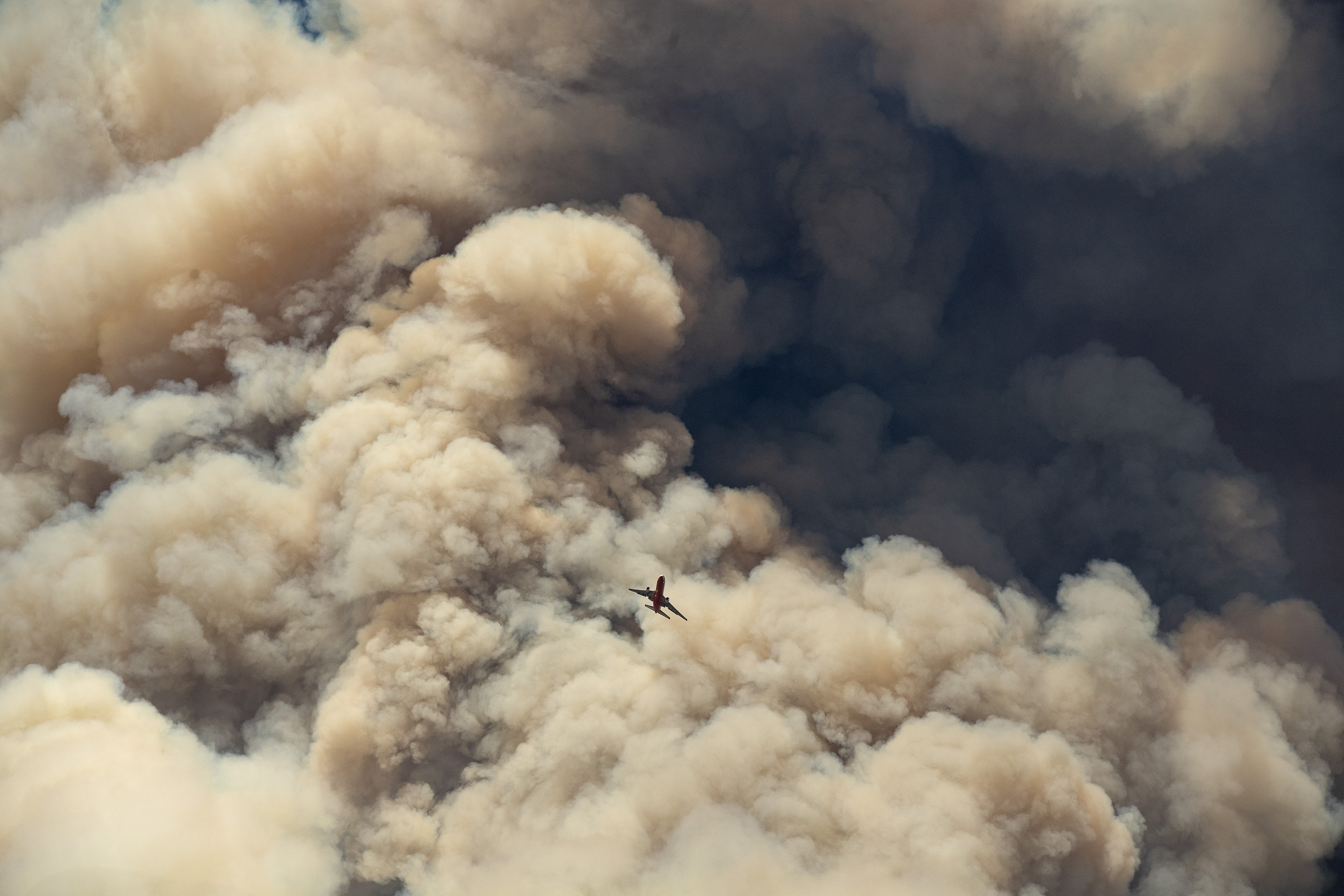 Un avión de extinción de incendios vuela lejos de una columna de ceniza de pirocumulus después de hacer una caída retardante en una cresta mientras los bomberos continúan luchando contra el incendio de Apple cerca de Banning, California (AFP)