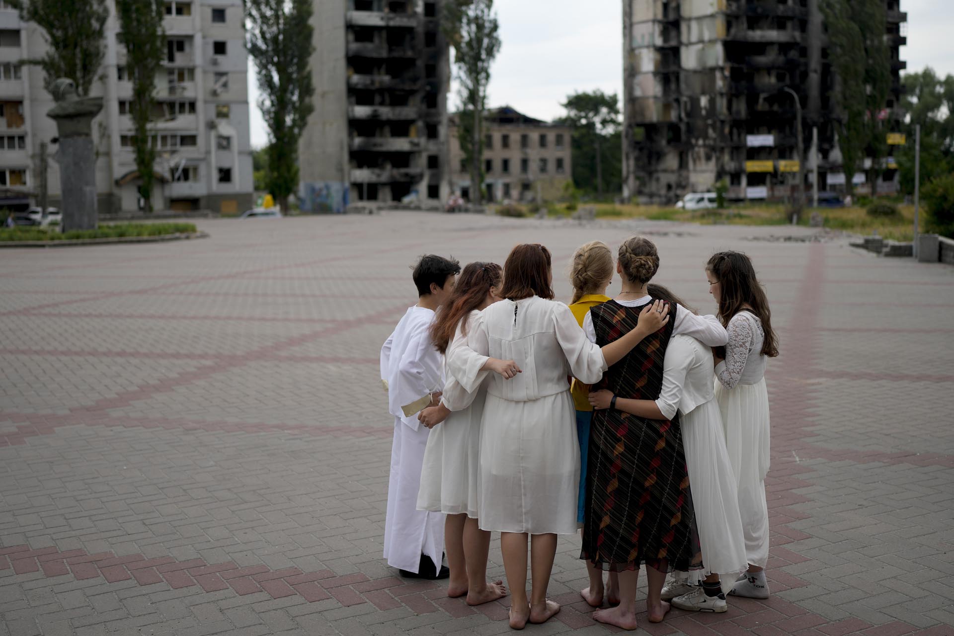 Jóvenes reunidos en un círculo mientras ensayan una representación cerca de un edificio dañado por ataques rusos en Borodyanka, a las afueras de Kiev, Ucrania, el martes 21 de junio de 2022. 