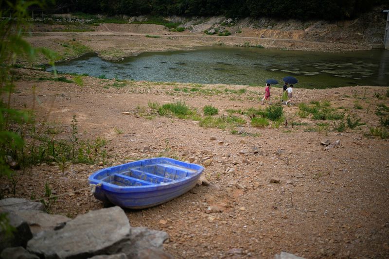 Un pequeño bote y varias personas en el lecho seco de un embalse, durante la ola de calor y la sequía en la cuenca del río Yangtsé, en Changxing, provincia de Zhejiang, China, el 20 de agosto de 2022. REUTERS/Aly Song