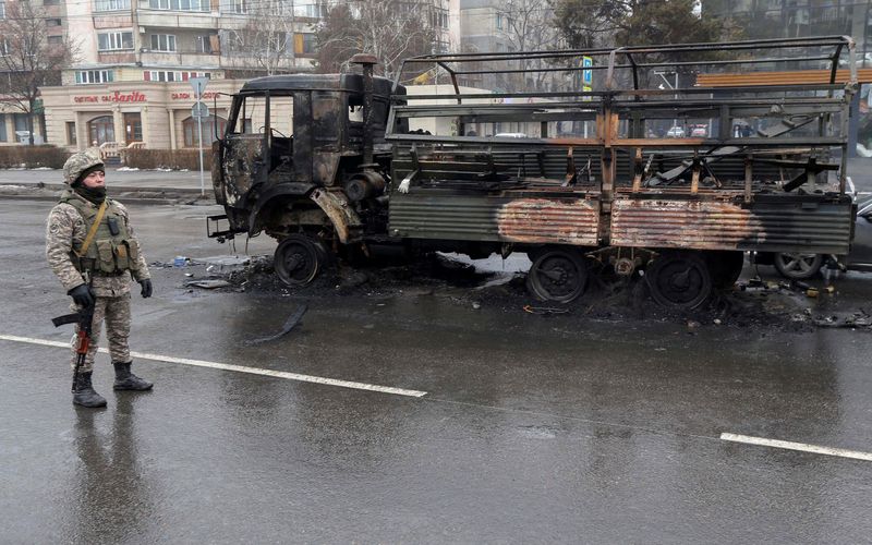 Un agente policial kazado hace guardia cerca de un camión quemado, mientras revisa vehículos en una calle después de disturbios masivos provocados por un aumento de los precios del combustible Almaty