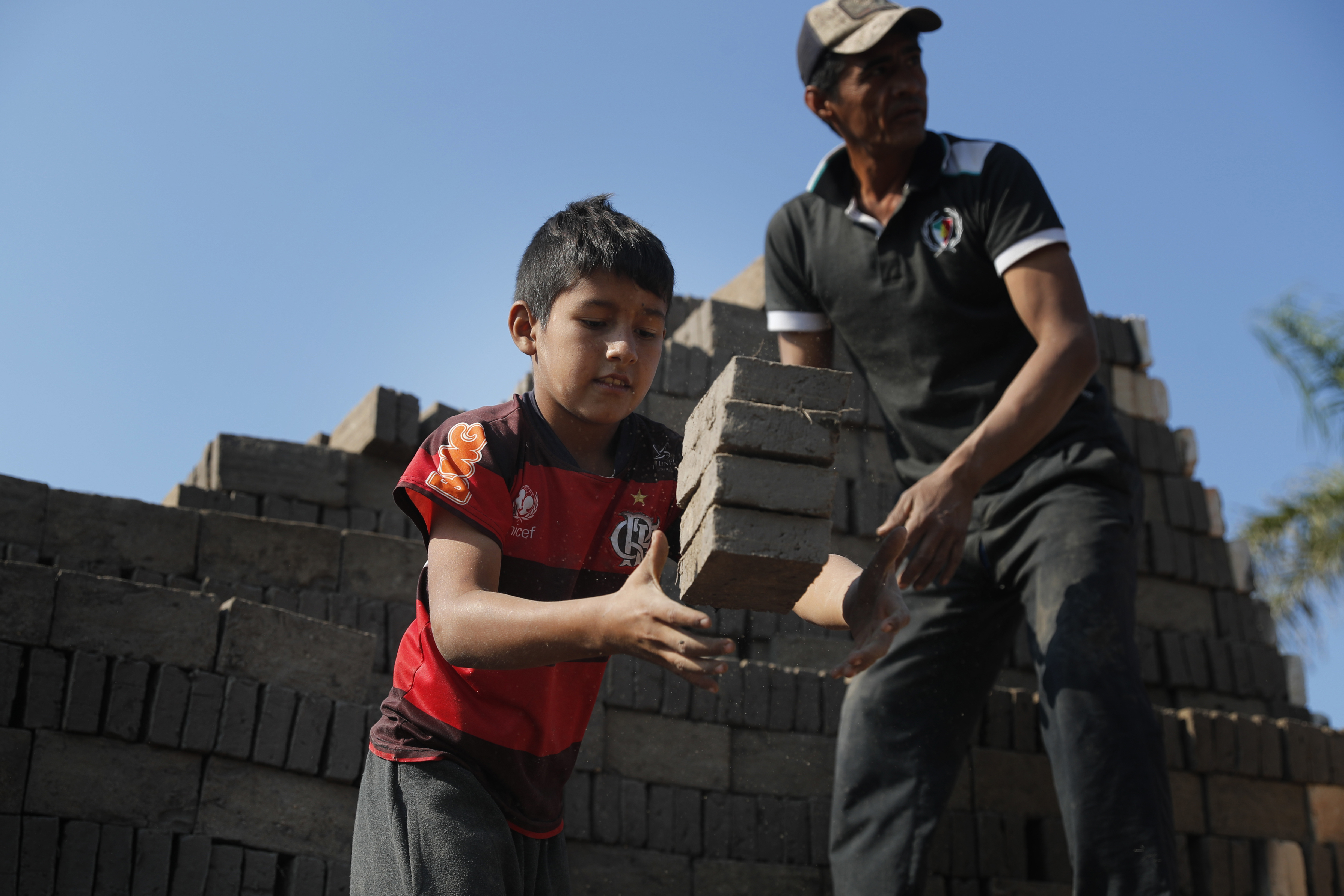 Alejandro, de 9 años, atrapa ladrillos para entregárselos a un hombre que los mete en el horno en una fábrica de ladrillos dirigida por sus tíos en Tobati, Paraguay, el lunes 31 de agosto de 2020.