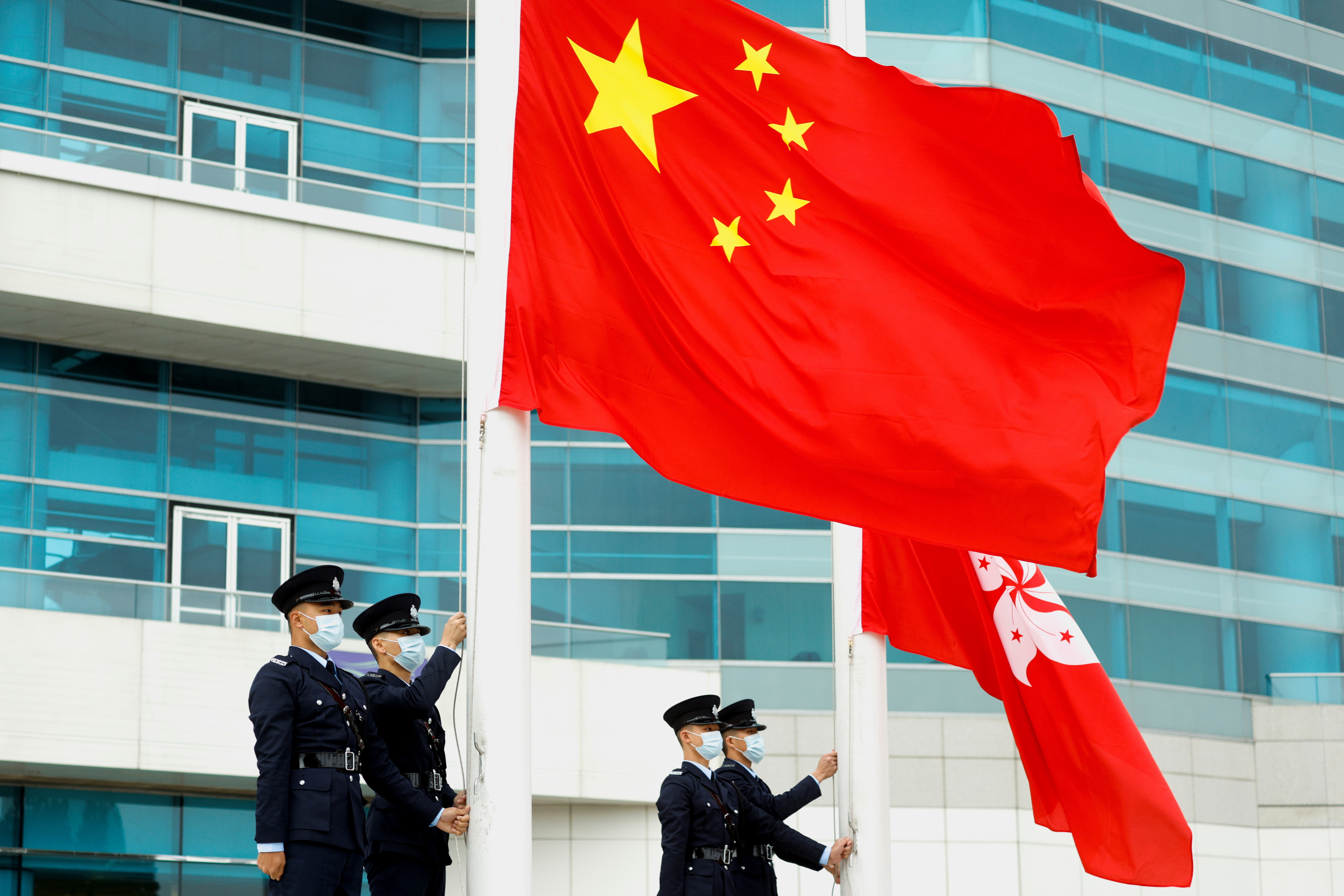 Agentes de policía izan las banderas de China y Hong Kong en una ceremonia en la plaza Golden Bauhinia, en Hong Kong, el 11 de marzo de 2021 (REUTERS/Tyrone Siu)