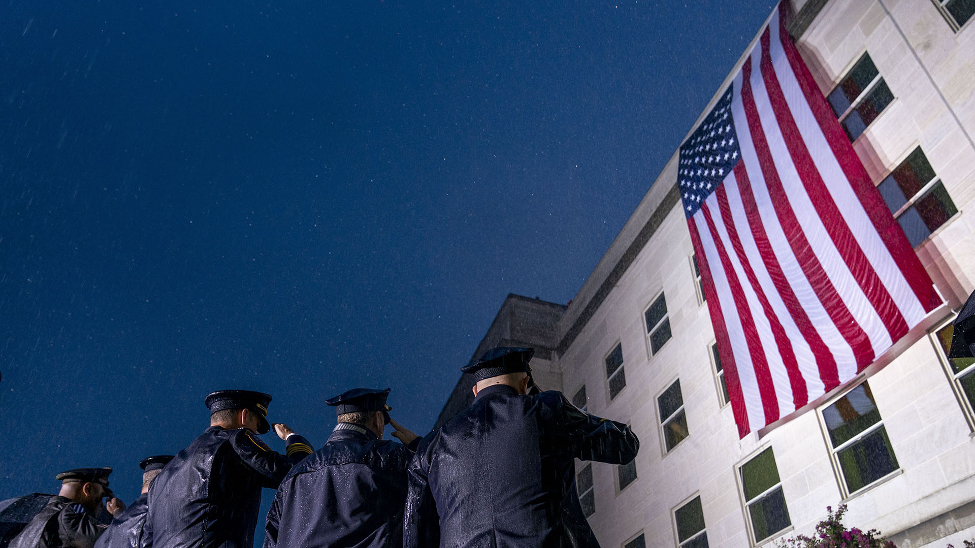 Los socorristas saludan bajo una lluvia torrencial mientras se despliega una bandera de los Estados Unidos en el Pentágono en Washington, el domingo 11 de septiembre de 2022, al amanecer de la mañana del 21 aniversario de los ataques terroristas del 9/11. (AP Photo/Andrew Harnik) 