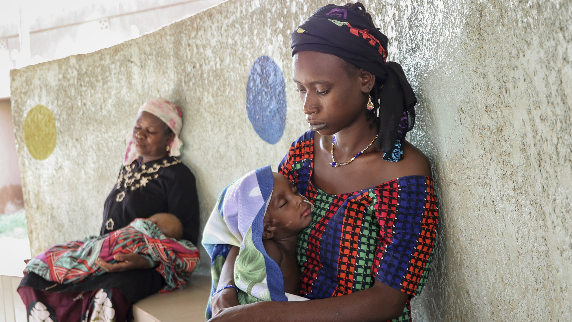Fatima Li, de 20 años, en primer plano, sostiene a su hijo de dos años, Hama Sow, mientras es tratado con una sonda de alimentación para la desnutrición, mientras Hadiara Ouedraogo, a la izquierda, se sienta con su nieta, Fatimata Ouedrago, de 2 años, que tiene un edema debido a una grave desnutrición, en la Universidad Yalgado Ouedraogo de Uagadugú (Burkina Faso) (AP Photo/Sam Mednick)