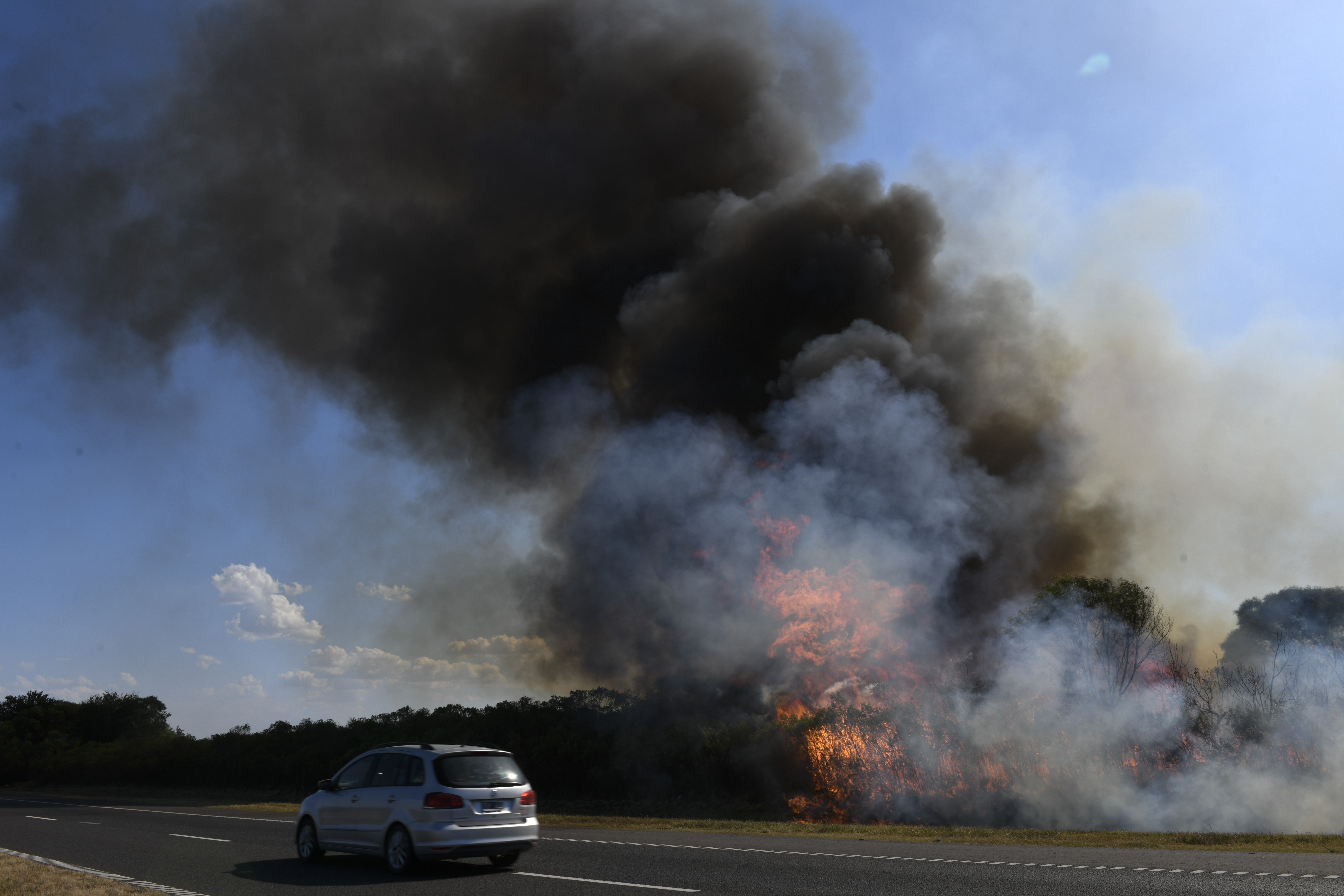 Un vehículo pasa al lado de los incendios de maleza en la autopista de Rosario-Santa Fe en Barrancas, en la provincia de Santa Fe, Argentina, el martes 17 de enero de 2023. (AP Foto/Gustavo Garello)