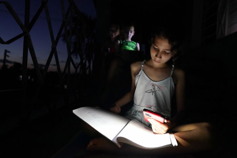 Emily Villega, de 10 años, hace sus deberes usando la luz de un teléfono móvil en el balcón de su casa durante un apagón en Guanajay, Cuba (REUTERS/Alexandre Meneghini)