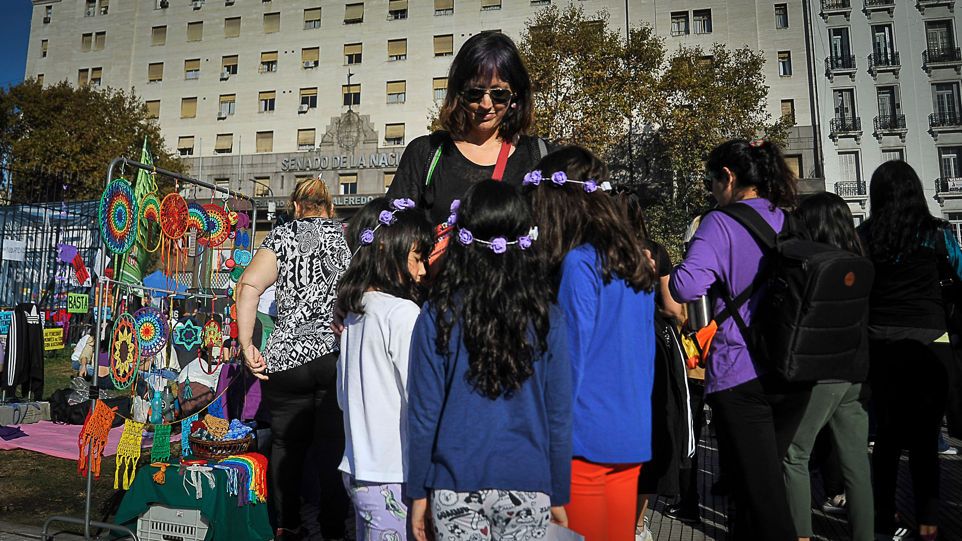Una mujer junto a tres niñas con vincha de flores violetas presentes en la marcha de Ni Una Menos