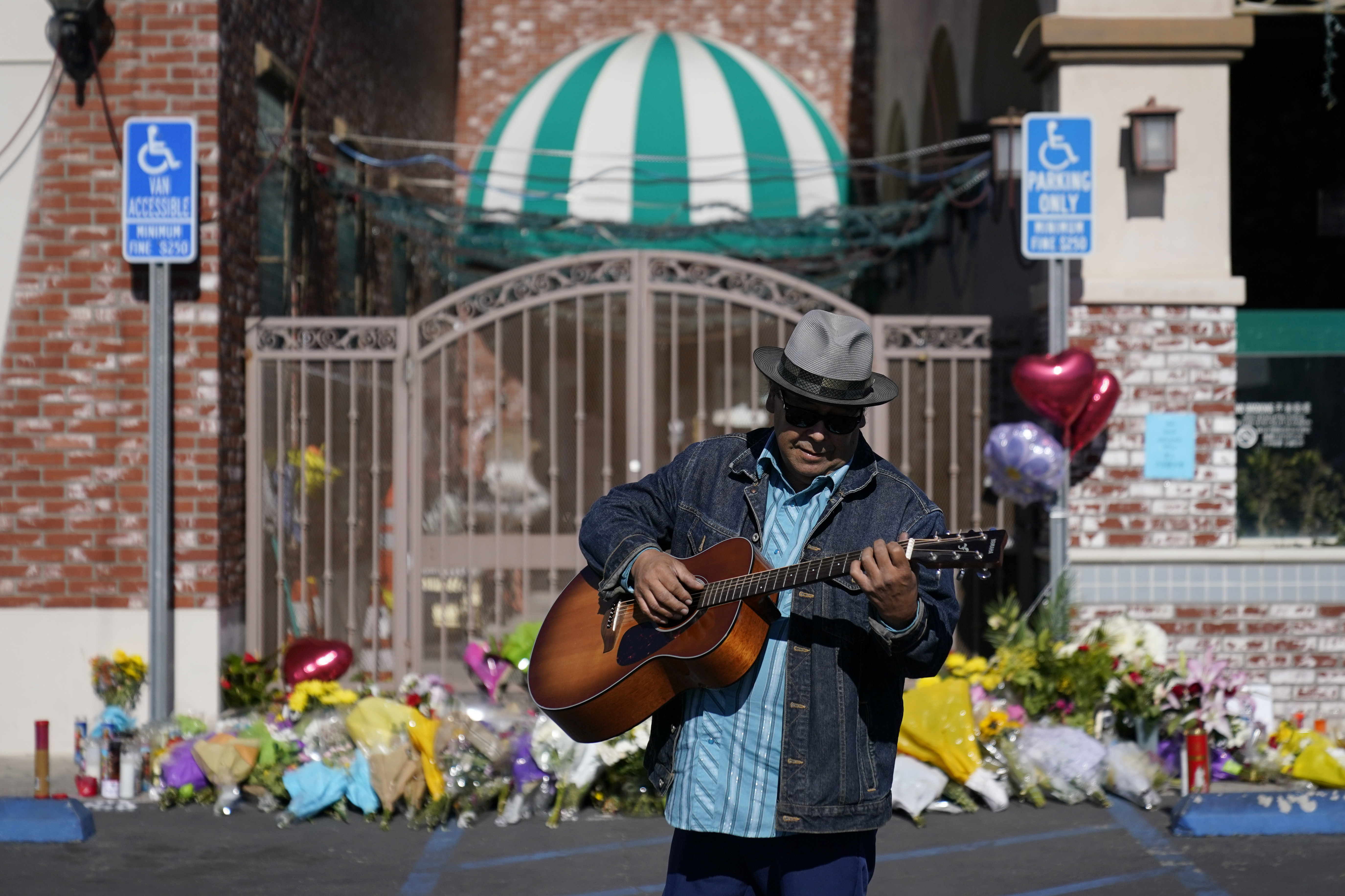 Gabriel Alexander plays guitar and sings in front of an impromptu offering outside the Star Ballroom Dance Studio, Tuesday, January 24, 2023, in Monterey Park, California.  (AP Photo/Ashley Landis)