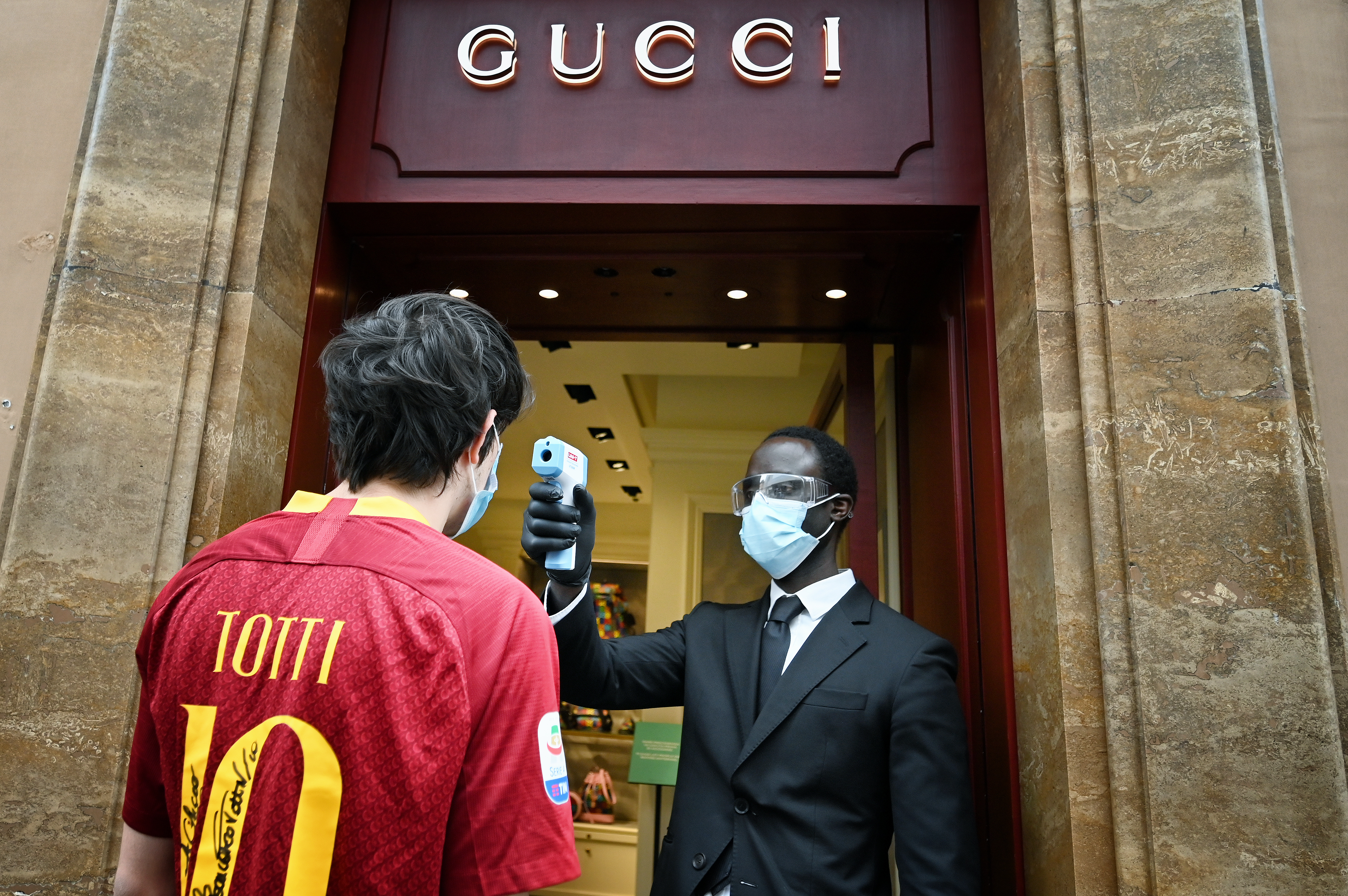 El empleado de una tienda de Gucci en Via dei Condotti, en Roma, mide la temperatura a un cliente. (Photo by Alberto PIZZOLI / AFP)