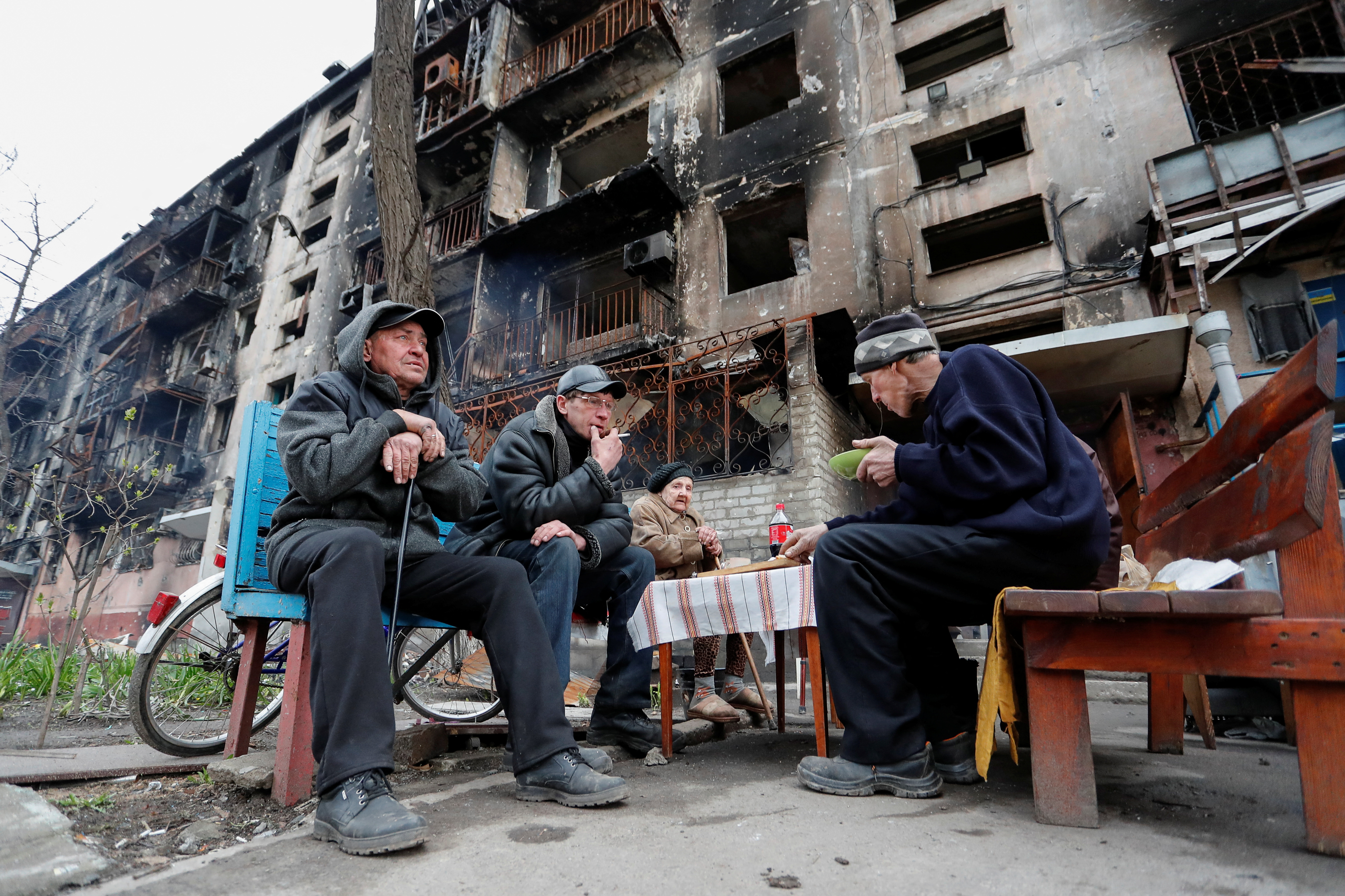 Residentes de Mariupol comparten una charla y algo de comida frente a un edificio destruido el 22 de abril