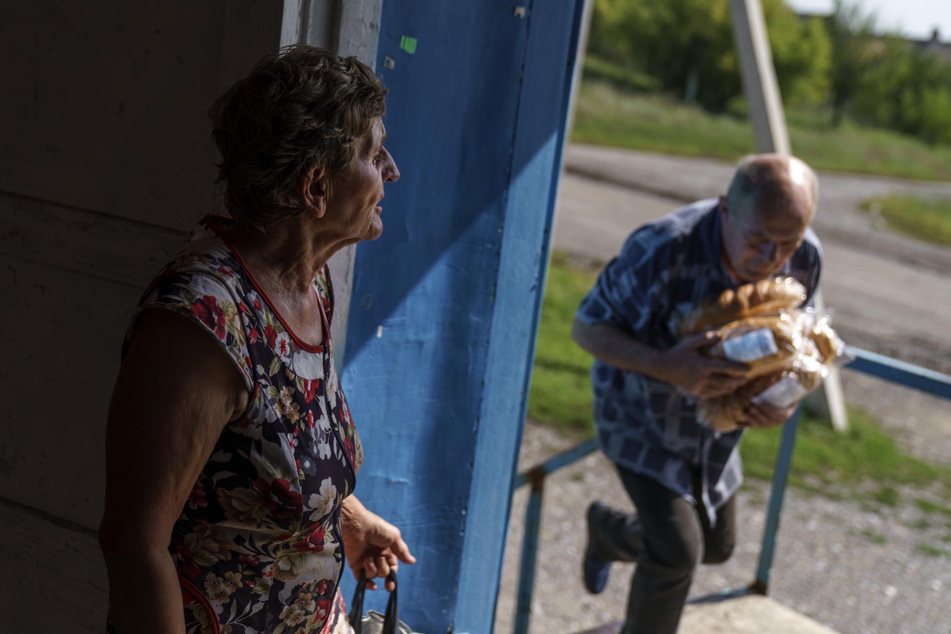 Vasyl Moiseienko, un jubilado, lleva pan fresco mientras una anciana espera la entrega en un comercio de Dyliivka, en la región de Donetsk, en el este de Ucrania, el sábado 20 de agosto de 2022. 