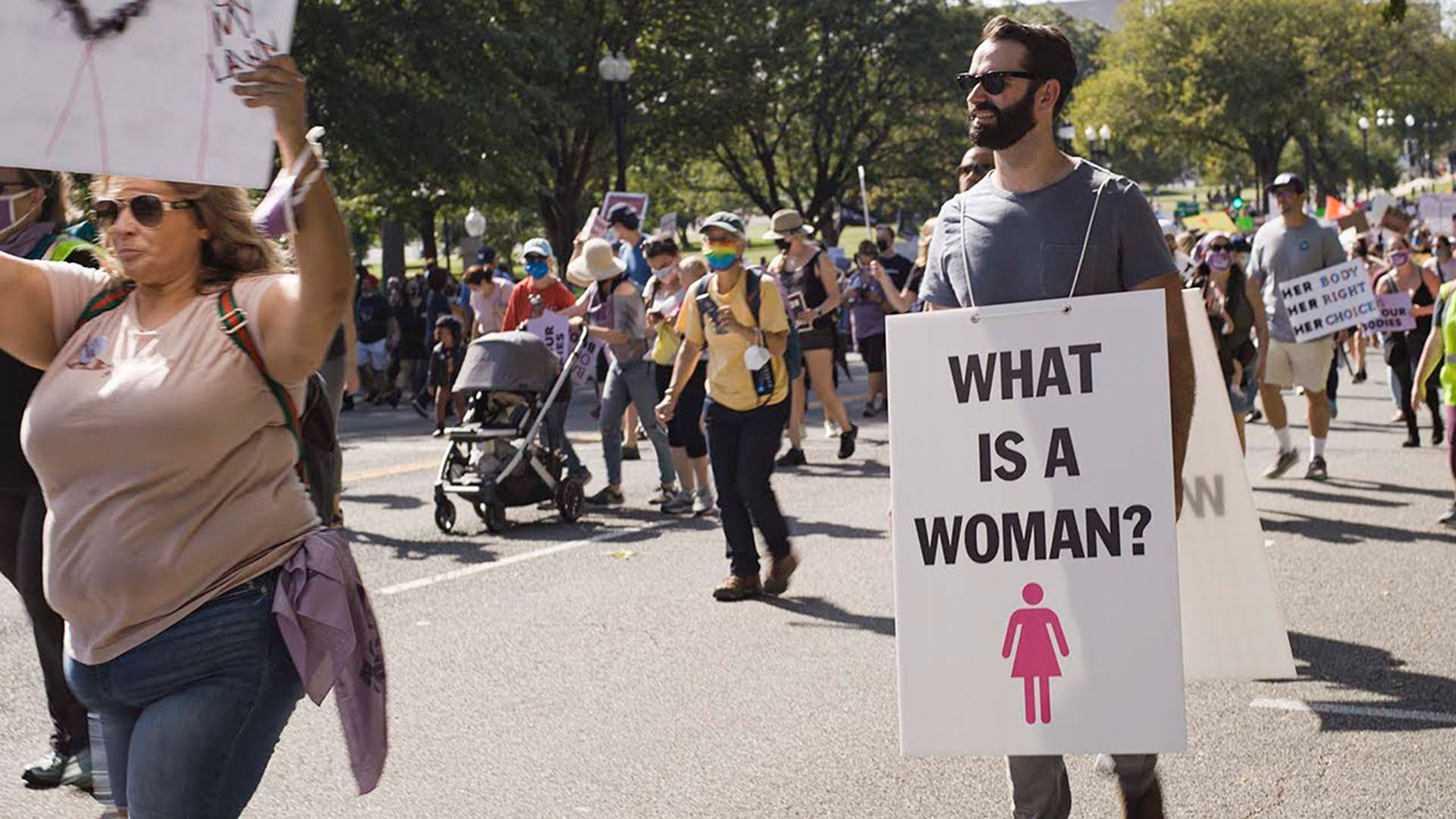 Matt Walsh, en una marcha de mujeres, con su pregunta en un cartel. Escena del documental "What is a woman?"