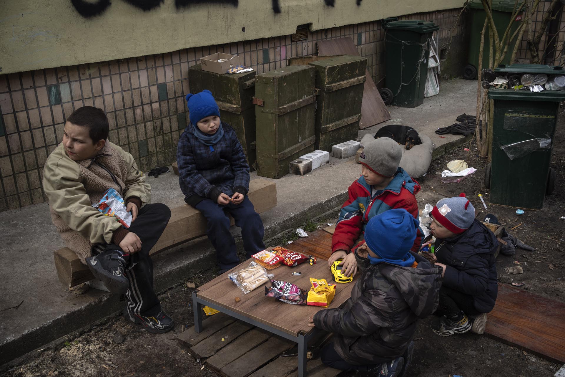 Niños sentados en torno a una mesa pequeña con comida que recibieron en un reparto de comida gratuita en Bucha, a las afueras de Kiev, Ucrania, el viernes 8 de abril de 2022. Un graffiti escrito por los vecinos en la pared al fondo dice "Niños" para informar al ejército ruso de que muchos niños viven en el edificio.