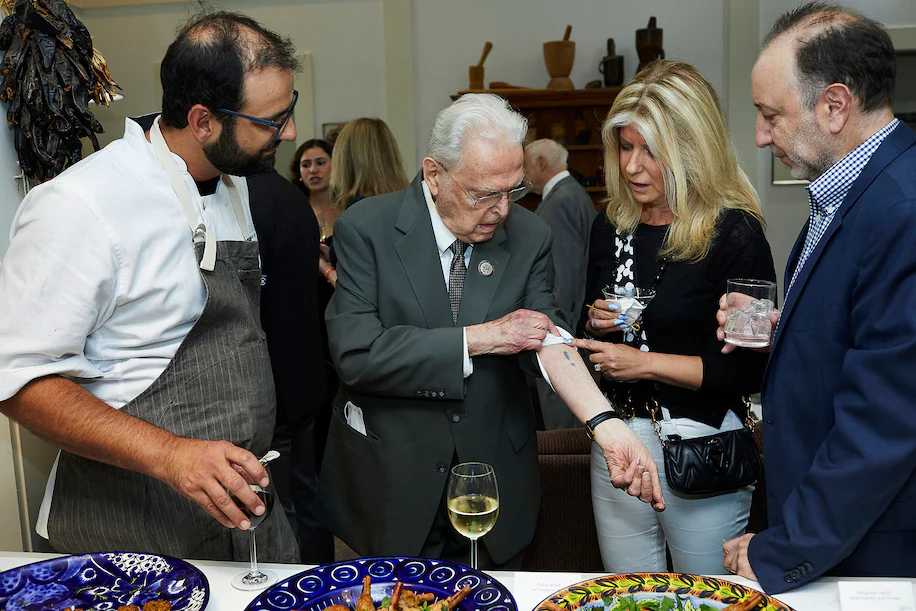 Steven Fenves, con el chef Alon Shaya, a la izquierda, en una recaudación de fondos en junio para el Museo Conmemorativo del Holocausto de EE. UU. Steven estaba mostrando un número de prisionero, tatuado en su brazo en Auschwitz, a los invitados Edye Fox Abrams y Steven Abrams. (Deb Lindsey para The Washington Post)