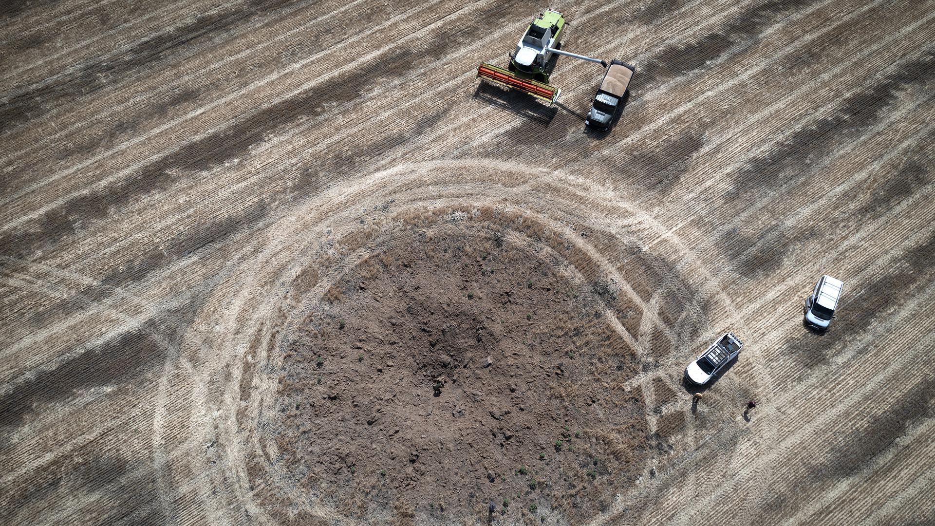 ARCHIVO - Un agricultor recoge la cosecha en un campo a diez kilómetros de la línea del frente, un cráter dejado por un cohete ruso en primer plano, en la región de Dnipropetrovsk, Ucrania, el 4 de julio de 2022.  (Foto AP/Efrem Lukatsky, archivo)

