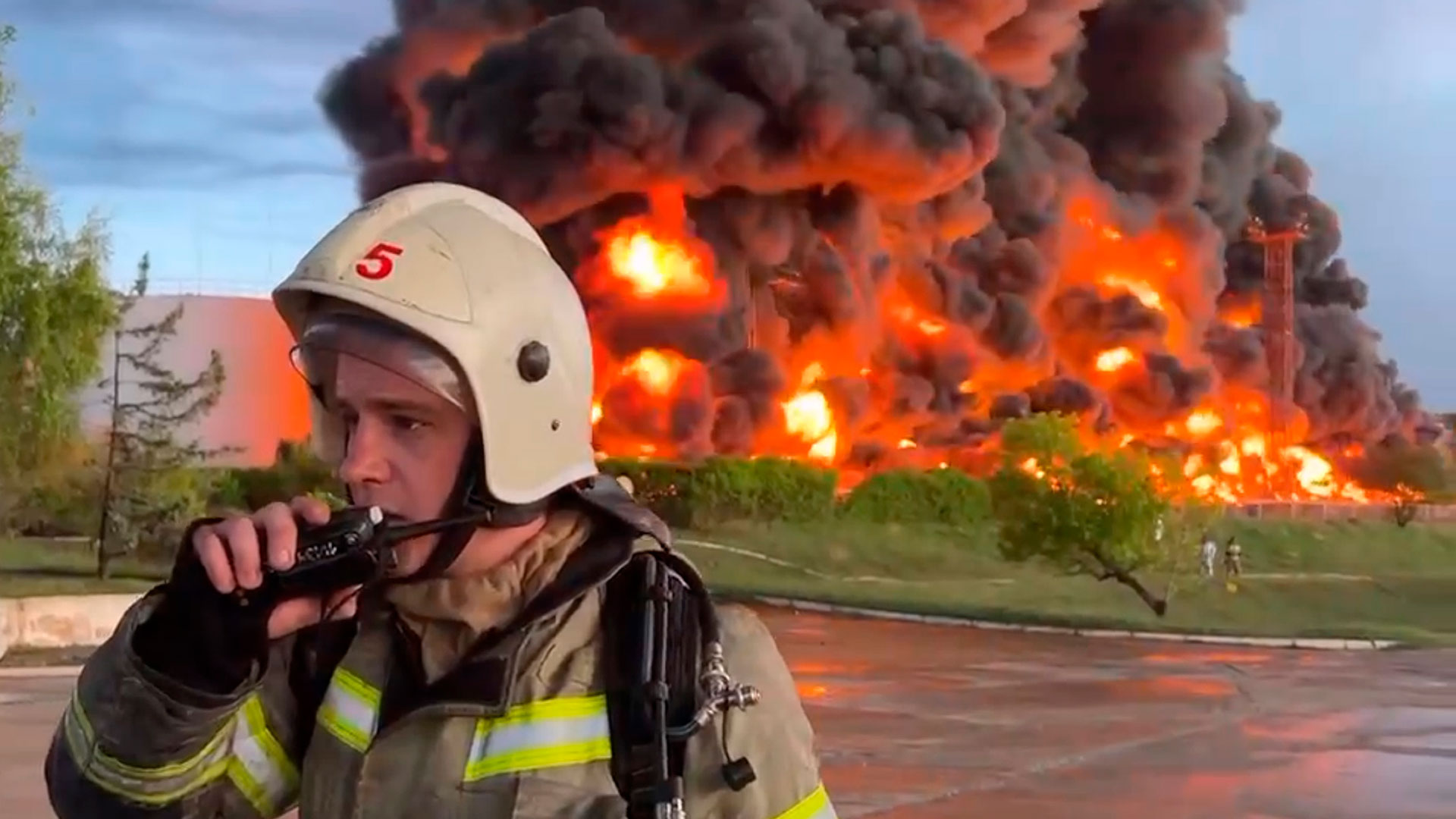 Un bombero habla por el walkie talkie mientras el humo y las llamas se elevan desde un depósito de combustible en llamas en Sebastopol, Crimea (AP)