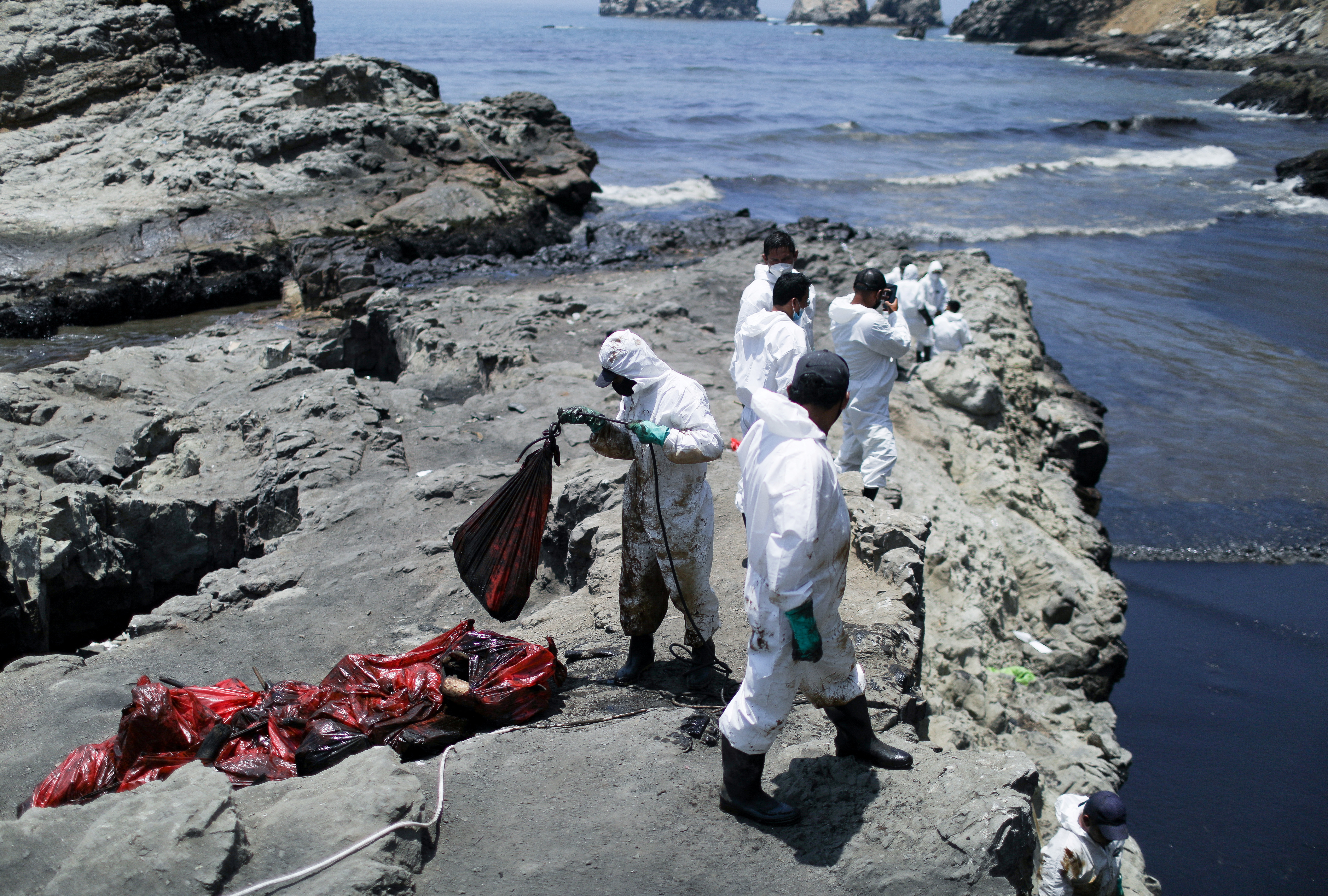 Workers clean up an oil spill caused by abnormal waves, triggered by a massive underwater volcanic eruption half a world away in Tonga, at the Peruvian beach in Ventanilla, Peru, 18 January 2022. REUTERS/Pilar Olivares