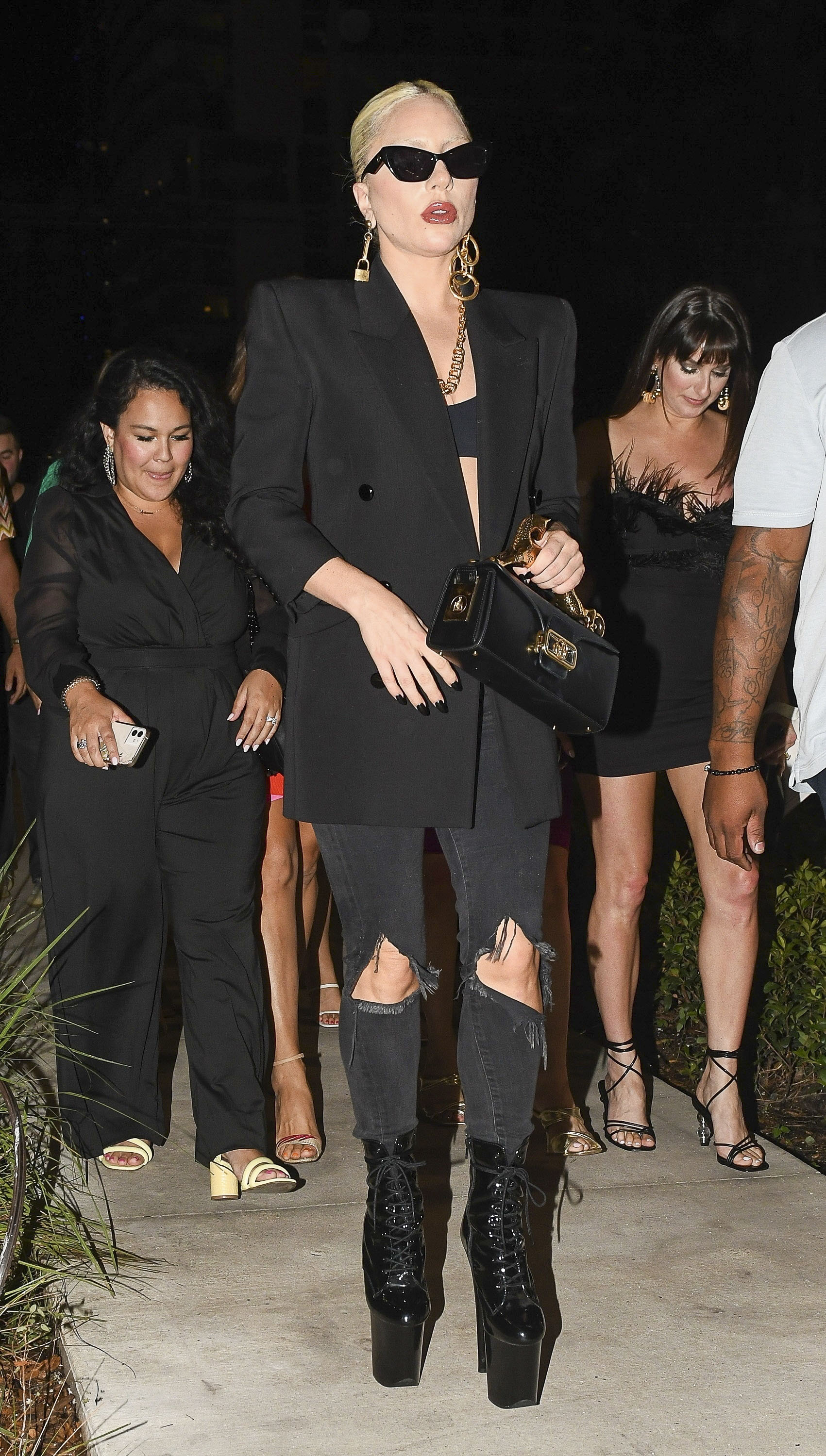 Lady Gaga increíble de negro con sus icónicas botas de plataforma mientras camina con amigos para ir a cenar en Miami