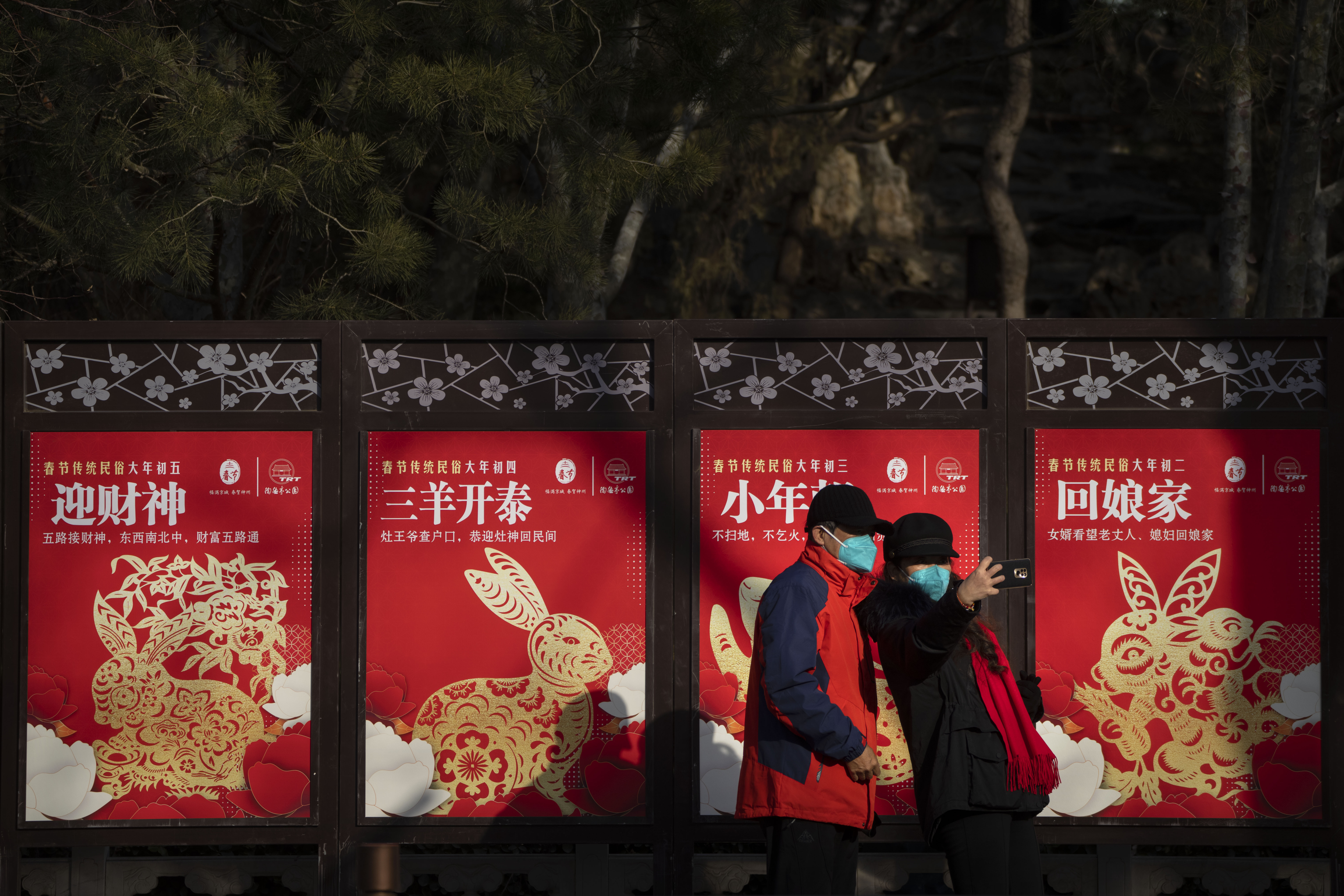 Visitantes con mascarilla posan ante varios carteles del Año del Conejo en un parque público en Beijing, el día de Año Nuevo del calendario lunar, el domingo 22 de enero de 2023. (AP Foto/Mark Schiefelbein)