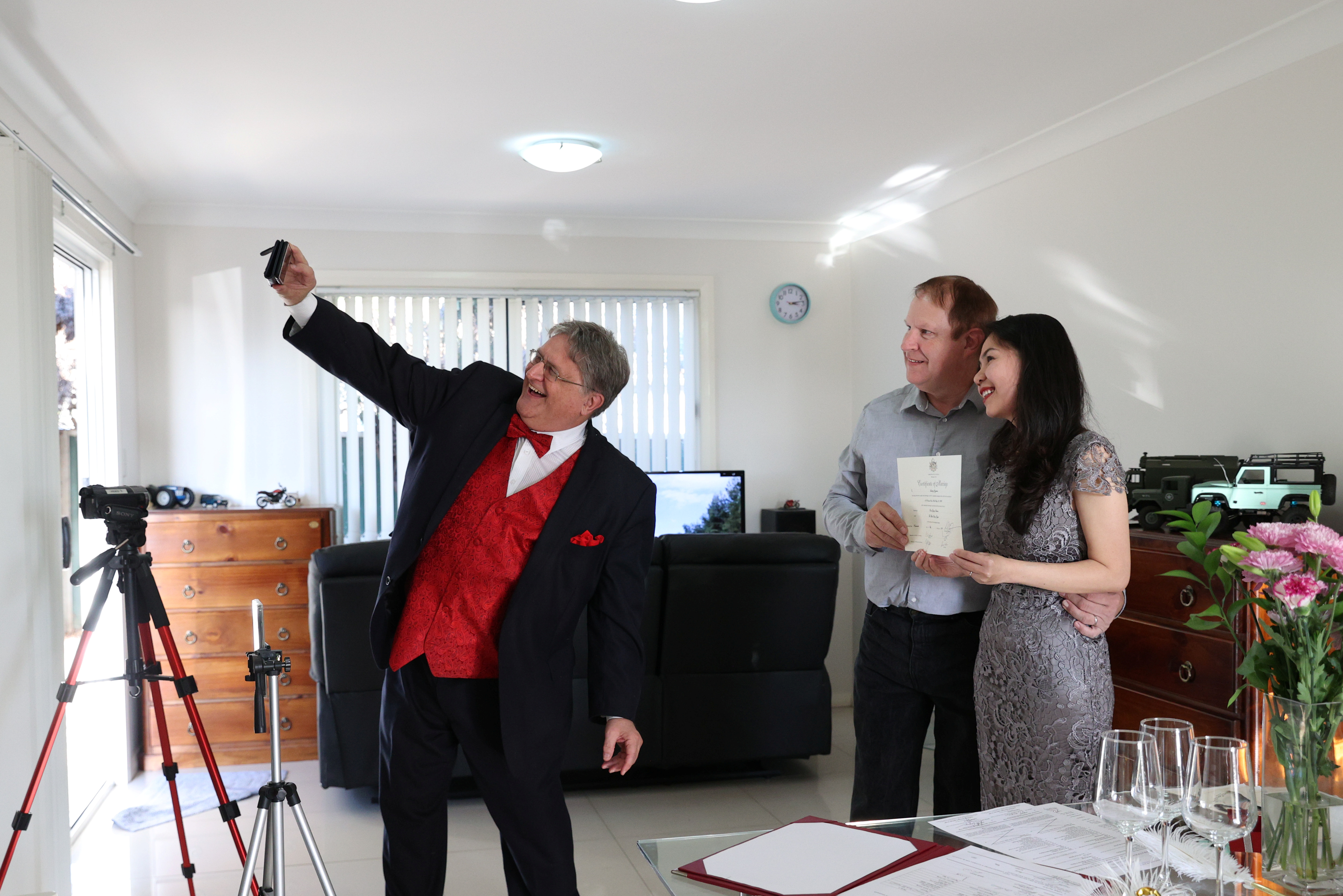 Lou Szymkow se toma una selfie con la pareja Peter Andrews y Hoang Nguyen después de oficiar una boda privada a el domicilio,  en Sydney, Australia (imagen tomada el 19 de mayo de 2020.  REUTERS/Loren Elliott)