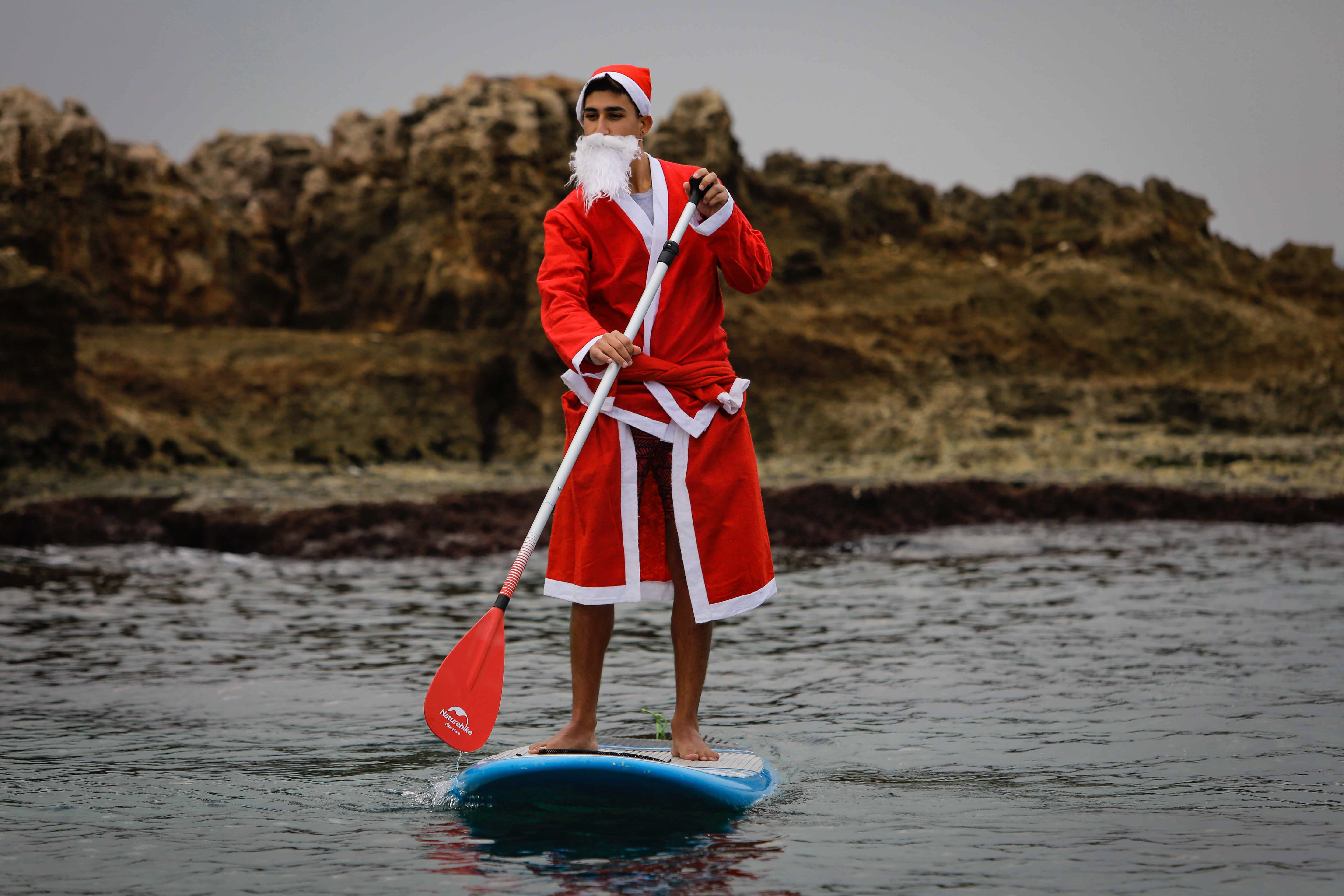 Un hombre libanés vestido con un traje de Papá Noel se pasea en un remo de pie en la ciudad costera de Batroun, en el norte del Líbano (Foto de Ibrahim Chalhoub / AFP)