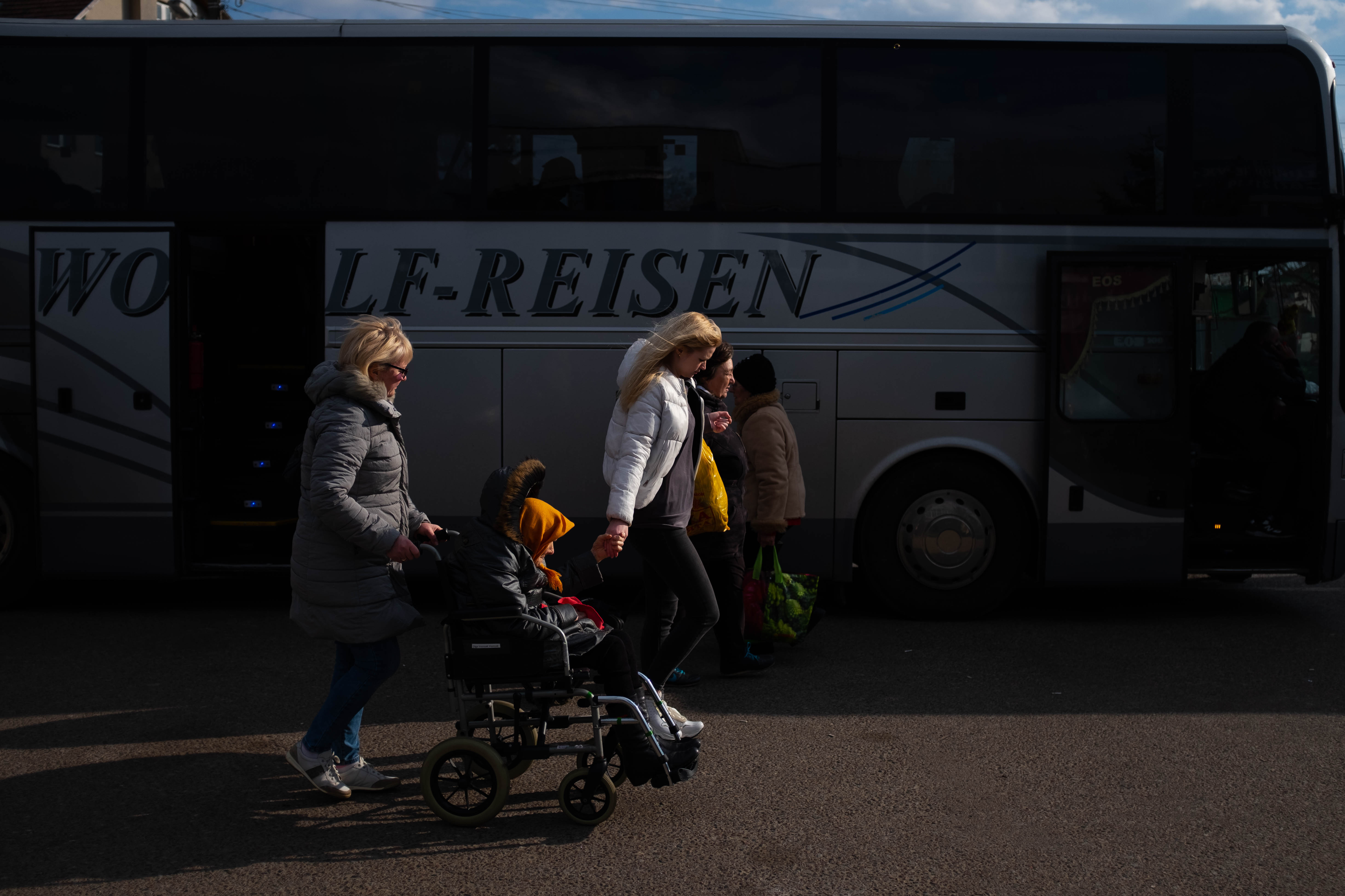 Una mujer mayor, acompañada por sus familiares, cruzan la frontera rumbo a Polonia.