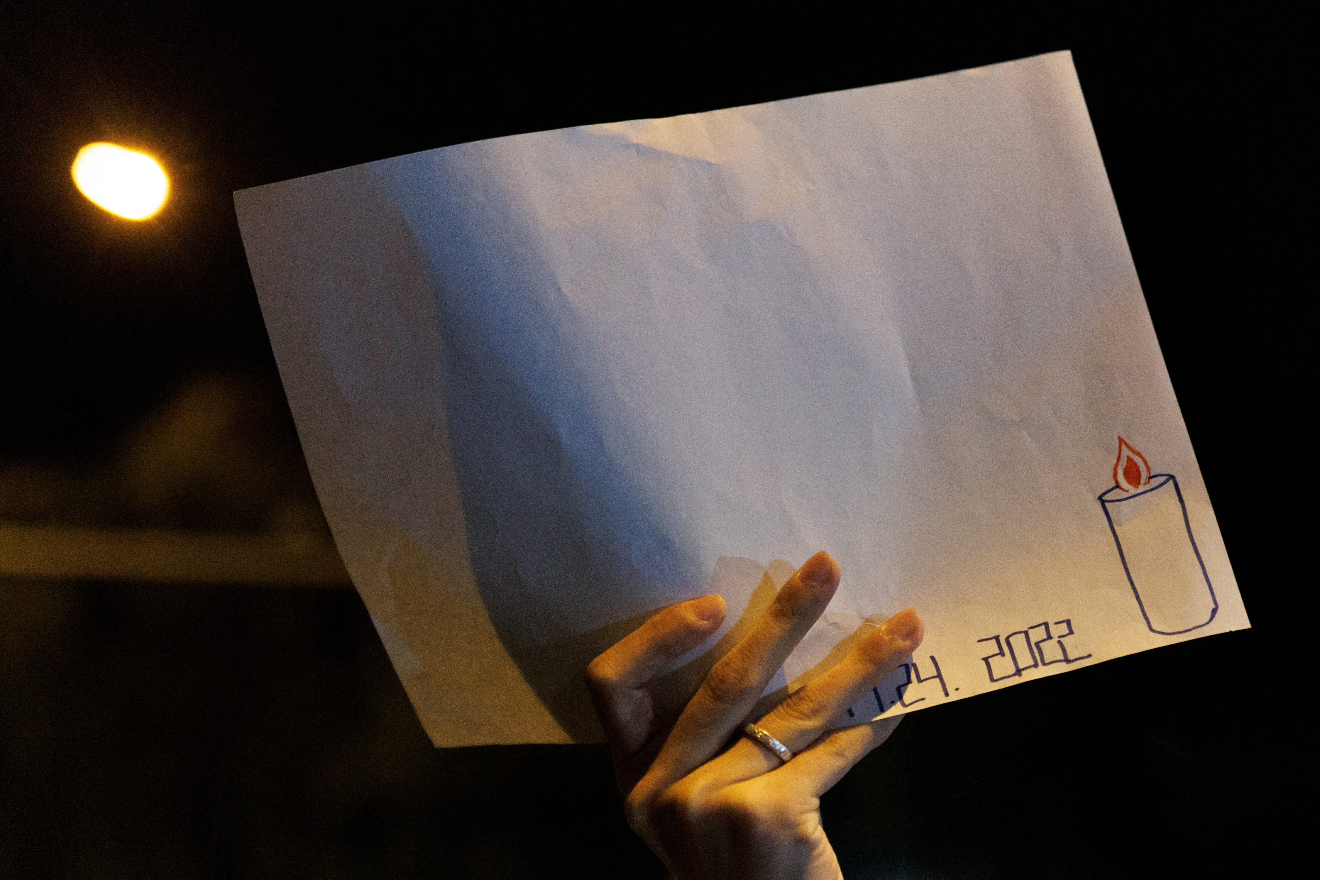 A woman holds a white sheet of paper with the date of a fire in Urumqi, during a commemoration of its victims, as outbreaks of the coronavirus disease (COVID-19) continue, in Beijing, China, November 27, 2022. REUTERS/Thomas Peter