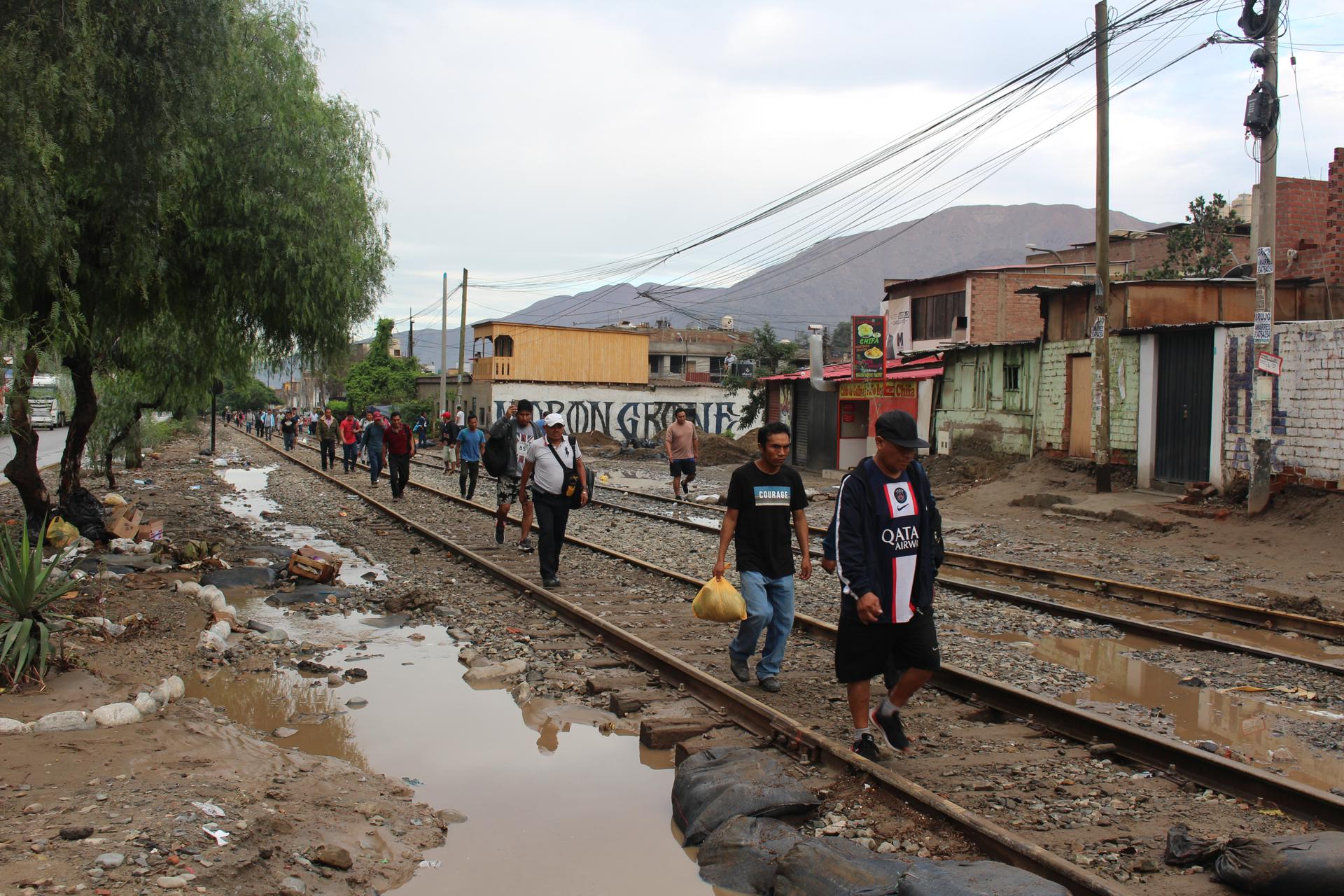 AME2421. LIMA (PERÚ), 15/03/2023.- Personas afectadas por las fuertes lluvias generadas por el ciclón Yaku caminan hoy en una vía férrea, en el distrito de Chaclacayo en Lima (Perú). Las intensas lluvias que cayeron en la madrugada de este miércoles en Lima por el ciclón "Yaku" han provocado deslizamientos de lodo e inundaciones en los distritos de Cieneguilla, Chosica, Chaclacayo, Ate, San Juan de Lurigancho, Carabayllo y Punta Hermosa, sin que hasta el momento se hayan reportado fallecidos. EFE/ Paula Bayarte
