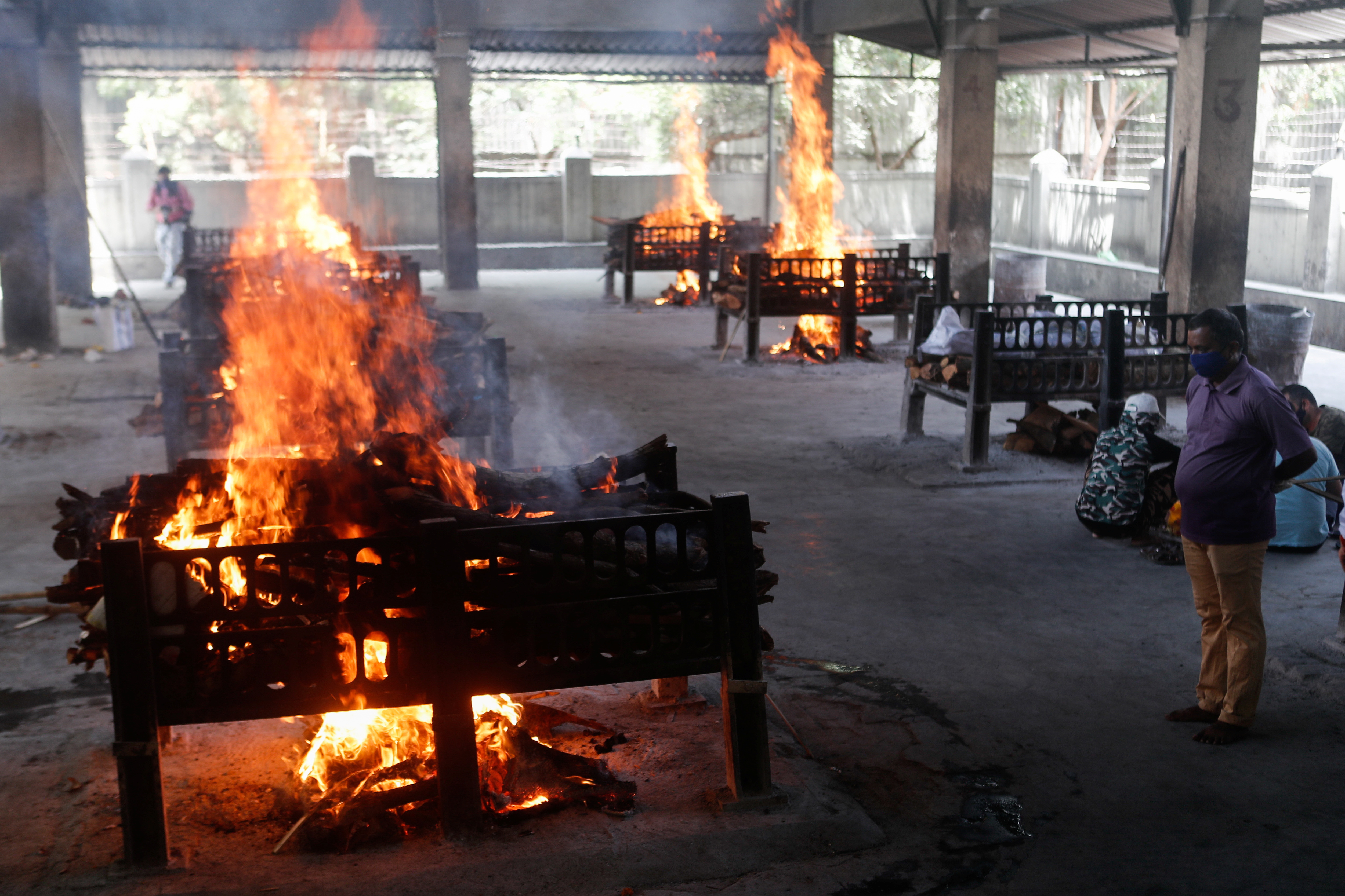 Un familiar de un paciente con coronavirus que falleció después de que un hospital se incendiara observa cómo se queman piras funerarias dentro de un crematorio en Virar, en las afueras de Mumbai, India (Reuters)