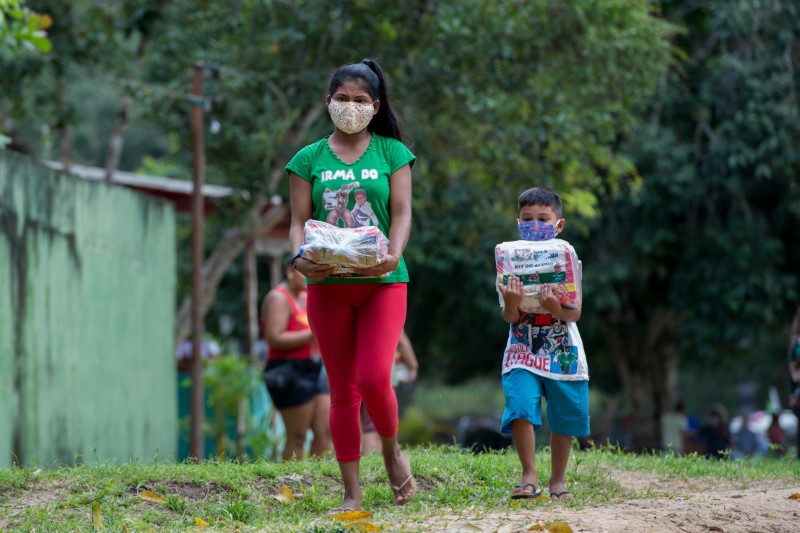 Una mujer joven y un niño llevan paquetes de ayuda alimentaria en una zona rural de de Manaos como parte del plan del gobierno brasileño para ayudar a las personas con bajos ingresos debido a la pandemia de coronavirus.