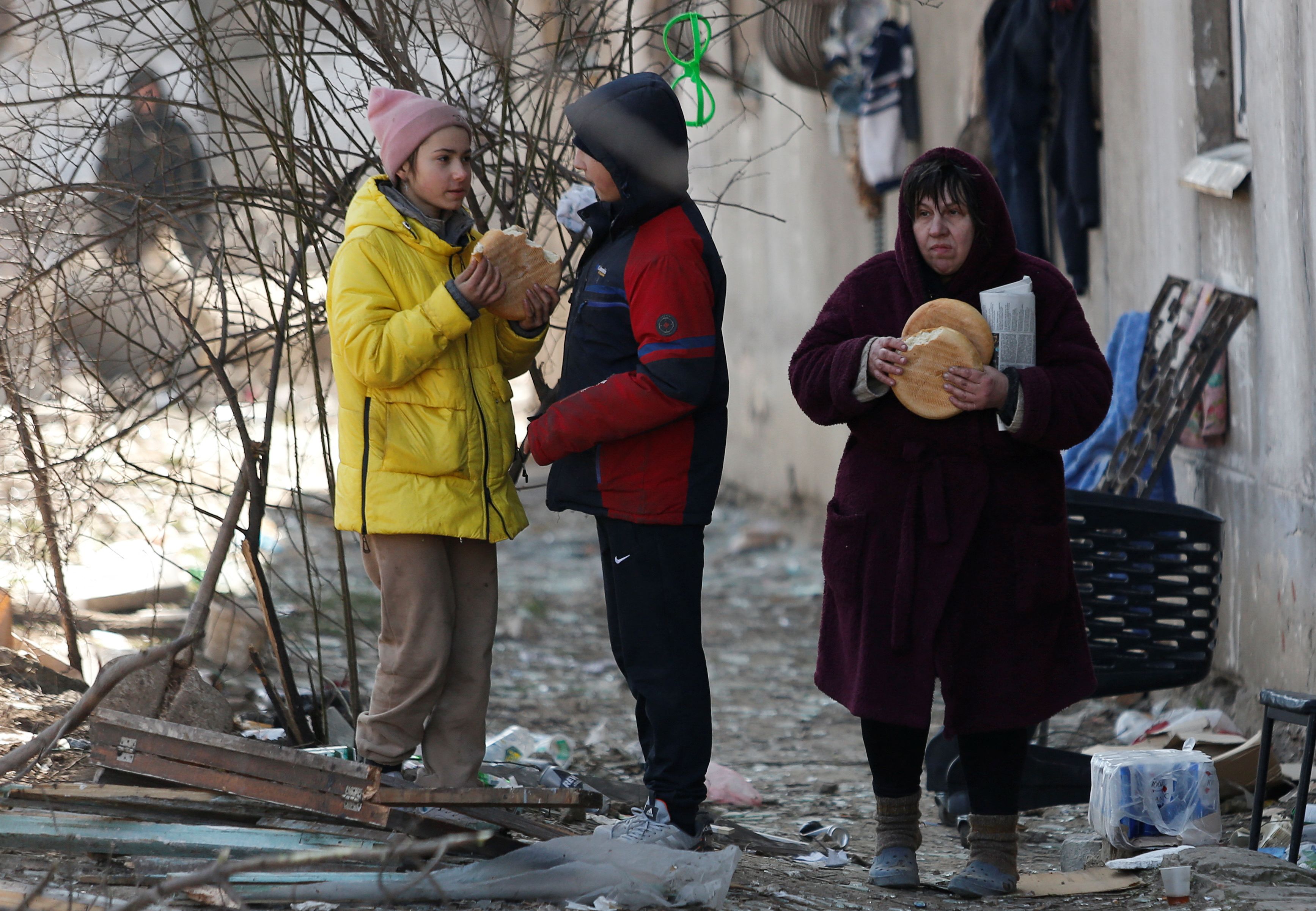 Local residents eat bread outside a building damaged in the course of Ukraine-Russia conflict in the besieged southern port city of Mariupol, Ukraine March 28, 2022. REUTERS/Alexander Ermochenko