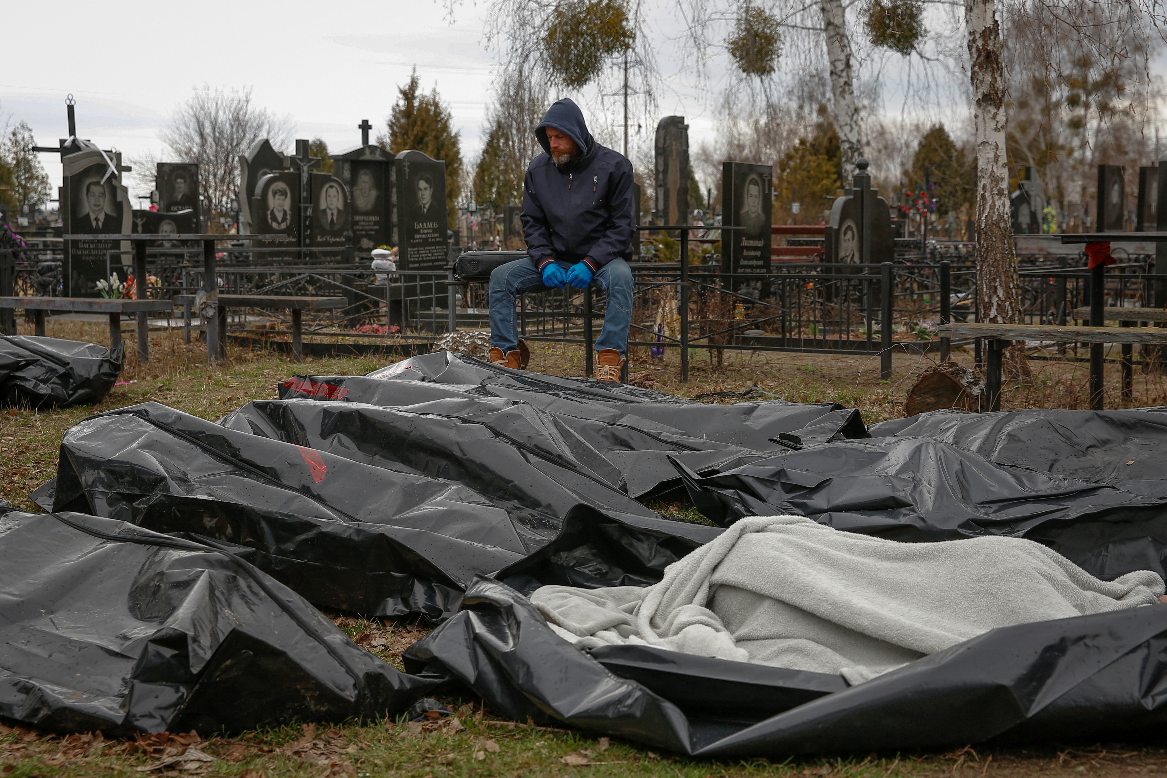 Un empleado del cementerio local, sentado cerca de los cadáveres de civiles que fueron recogidos de las calles en Bucha, en las afueras de Kiev. (REUTERS/Oleg Pereverzev)