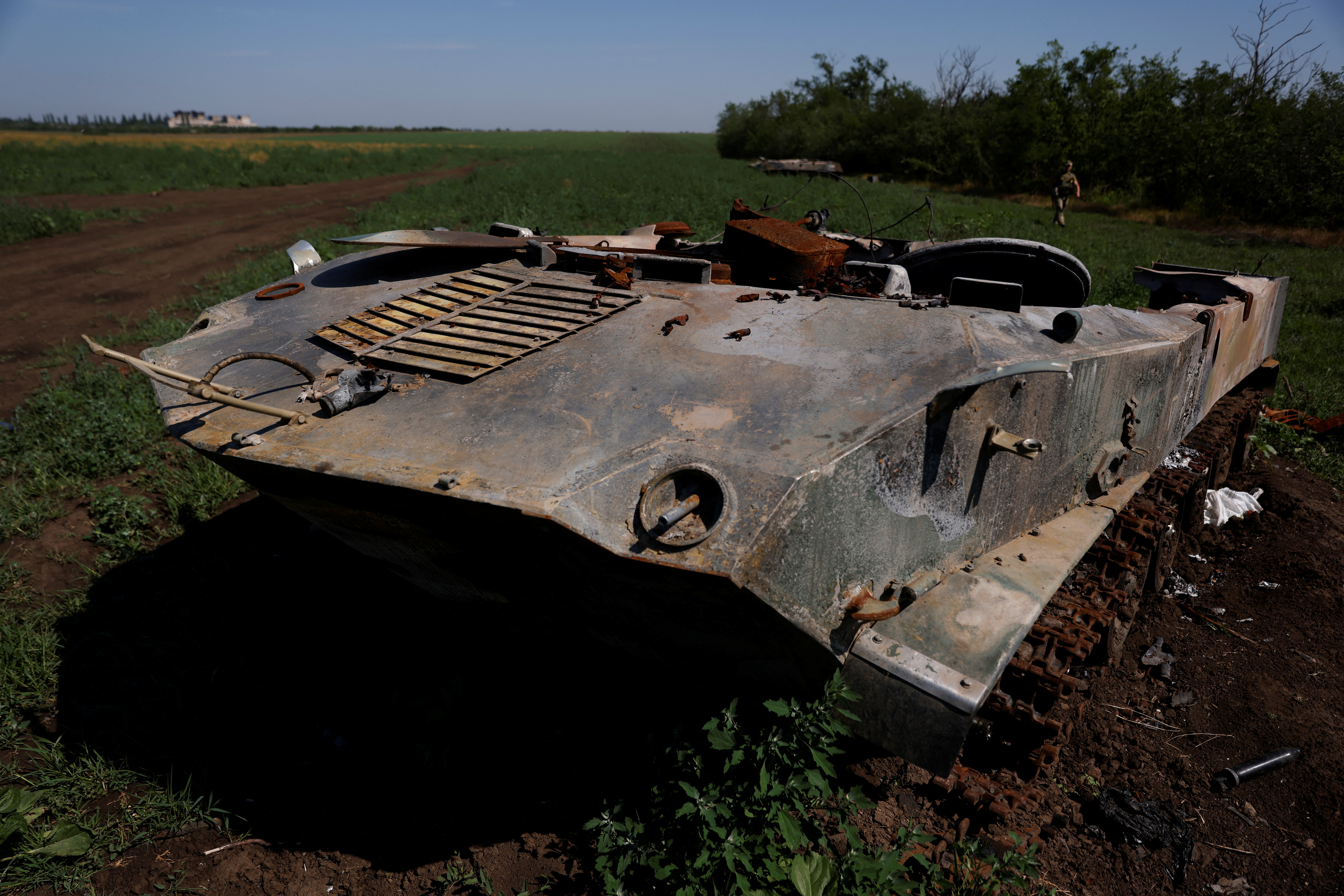 A Ukrainian soldier walks past a destroyed Russian tank in a field in the Mykolaiv region of Ukraine on June 12, 2022 (REUTERS/Edgar Su)