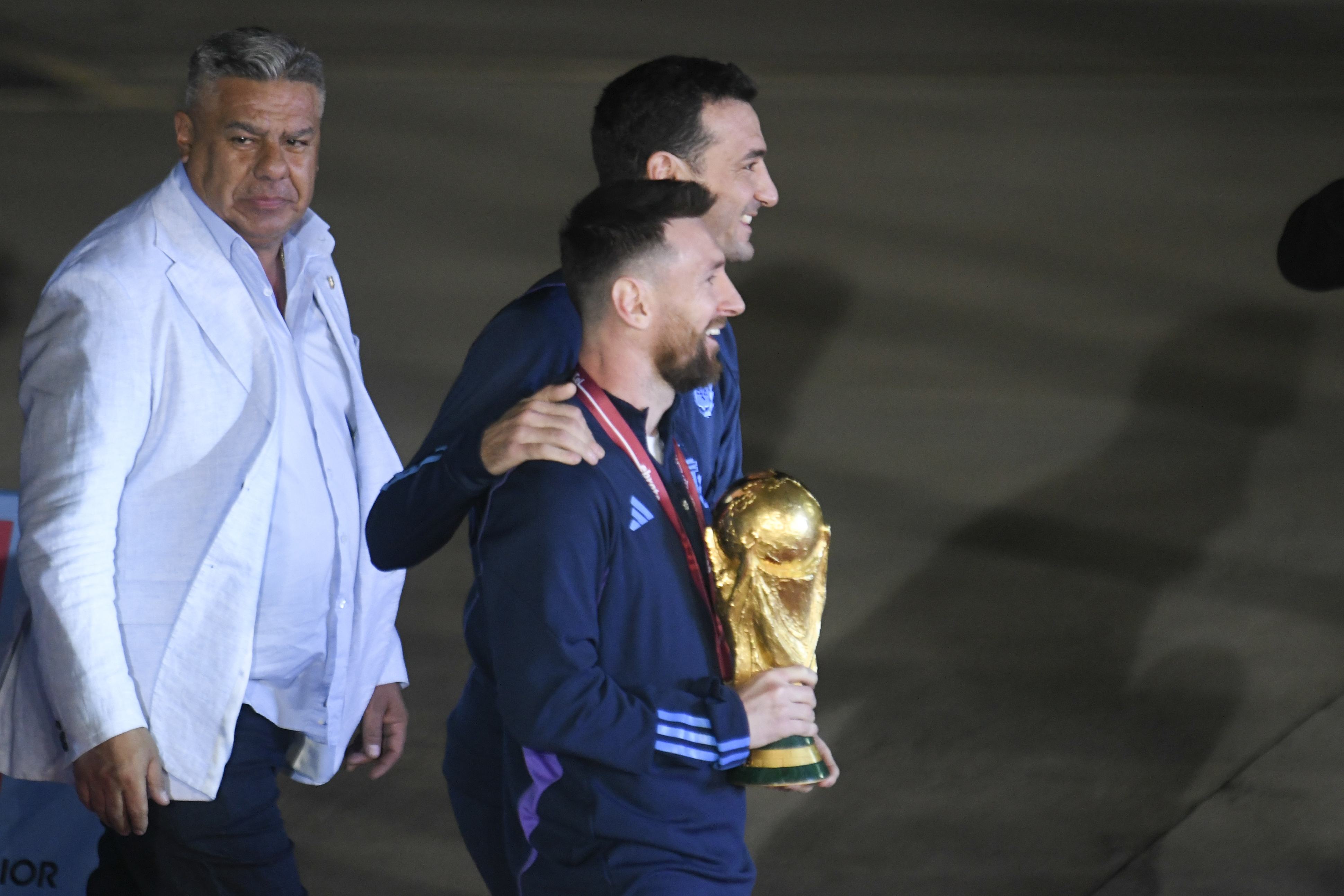 El capitán Lionel Messi lleva la copa, lo abraza el técnico Lionel Scaloni, detrás Claudio Chiqui Tapia, presidente de la AFA, segundos después de pisar suelo argentino tras volar desde Qatar