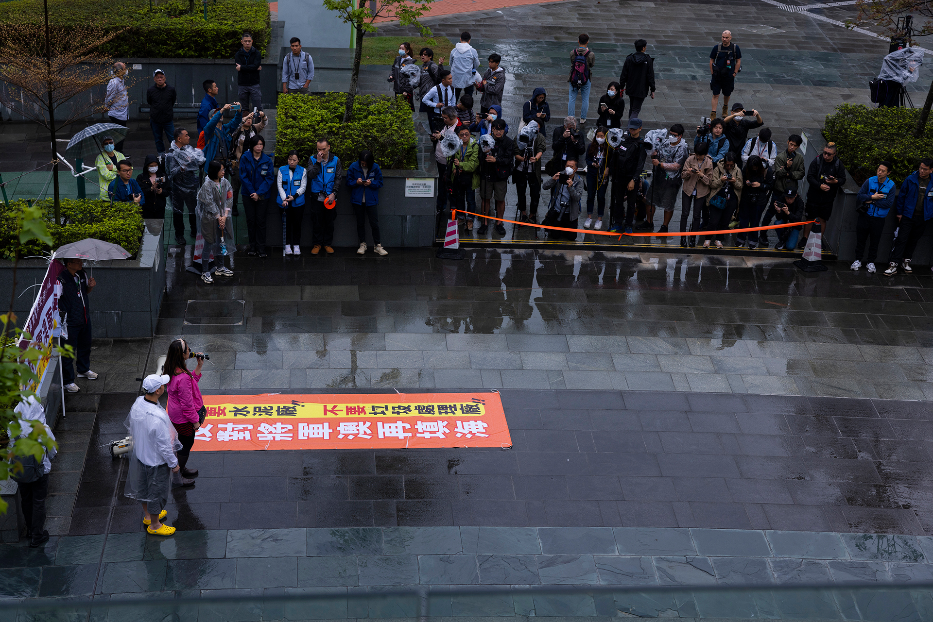 Los manifestantes, a la izquierda, organizan una manifestación como miembro de la prensa, a la derecha, de pie en un área acordonada en Hong Kong, el domingo 26 de marzo de 2023.  (AP Photo/Louise Delmotte)

