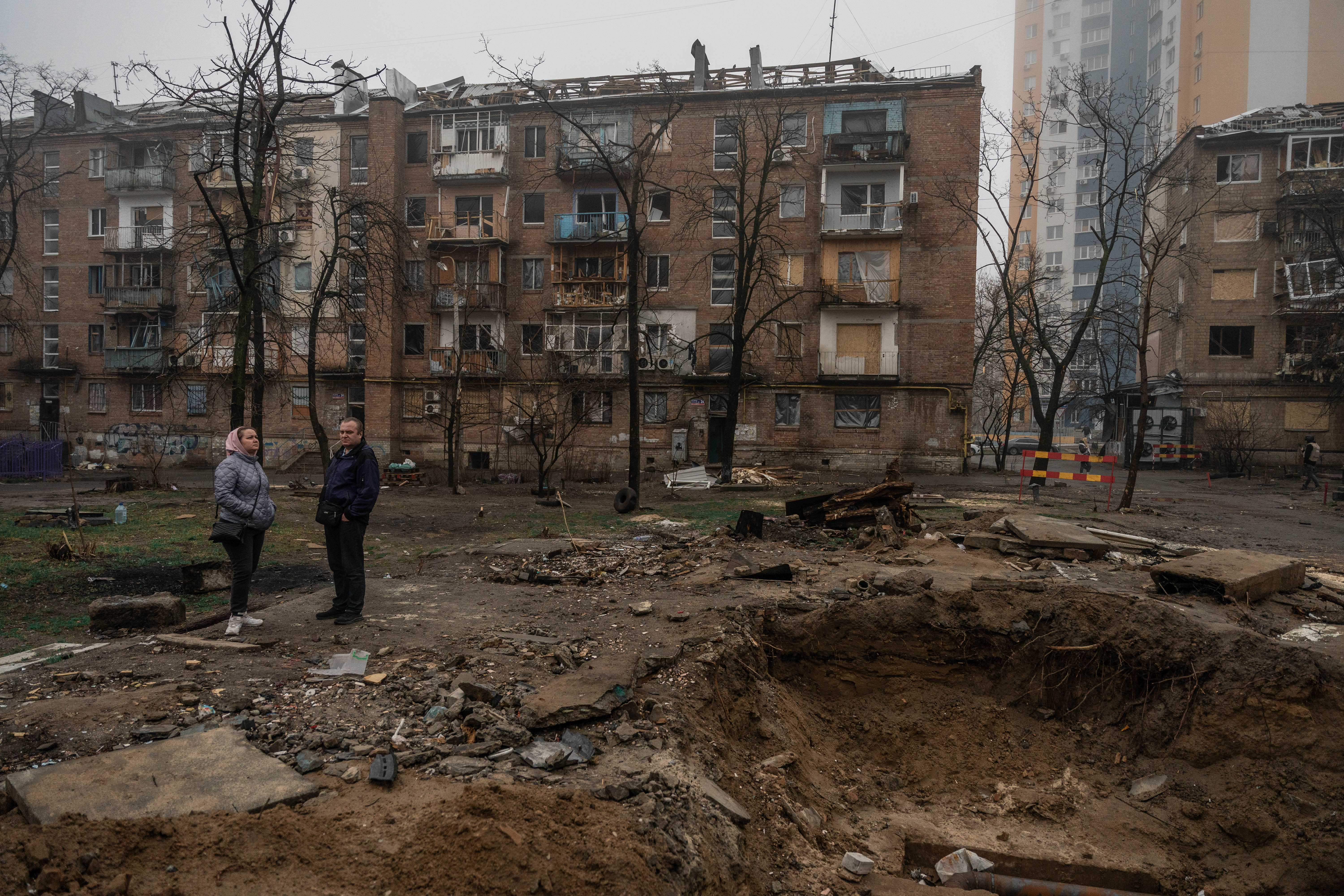 Vecinos de Podilskyi en Kyiv, se detienen a observar un crater de un misil que cayo en su barrio.