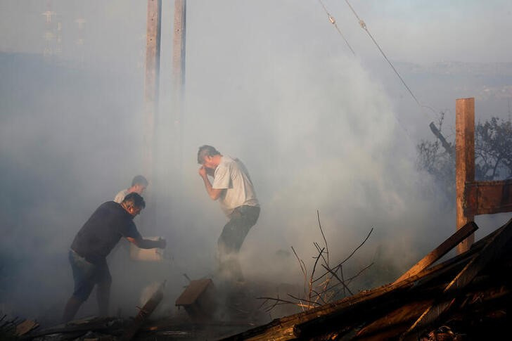 Un hombre vierte agua sobre los restos de una casa quemada durante un incendio forestal en Viña del Mar (REUTERS/Rodrigo Garrido)