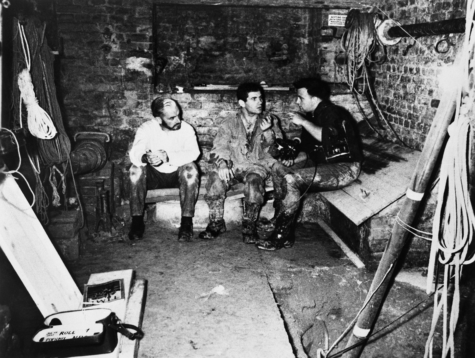 El corresponsal de NBC News, Piers Anderton (izquierda), y el camarógrafo de NBC News, Peter Dehmel (derecha), hablan recientemente con el estudiante de Berlín Occidental, Dominico Sesta, en el sótano de un edificio en Berlín Occidental. Sesta es uno de un grupo de estudiantes de Berlín Occidental que cavó un túnel de escape desde el edificio que se muestra, 450 pies hacia Berlín Oriental, pasando por debajo del Muro Comunista. (Foto de Bettmann Archive/Getty Images)
