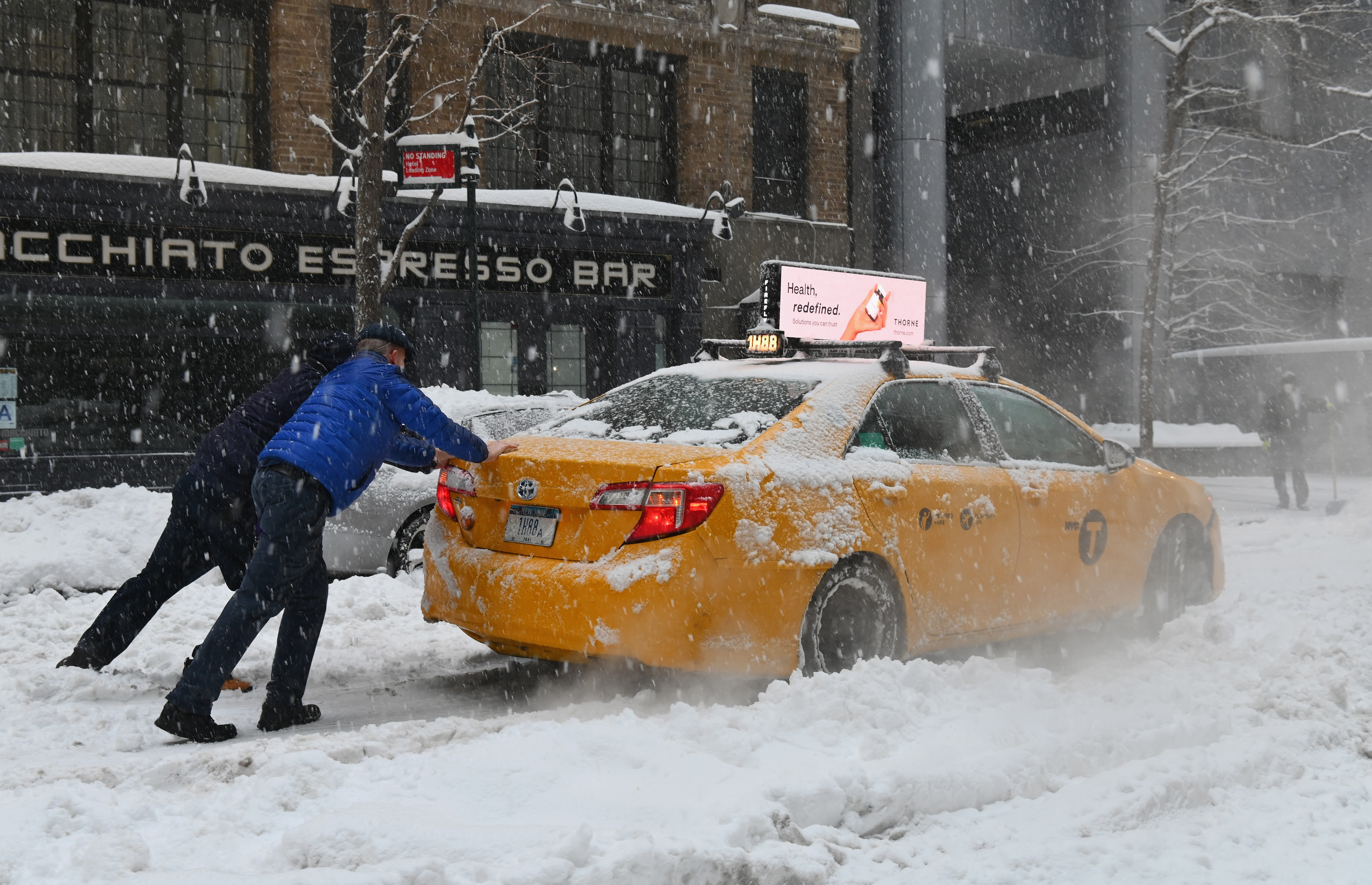 Dos personas empujan un taxi varado en la nieve en Nueva York (Angela Weiss / AFP)