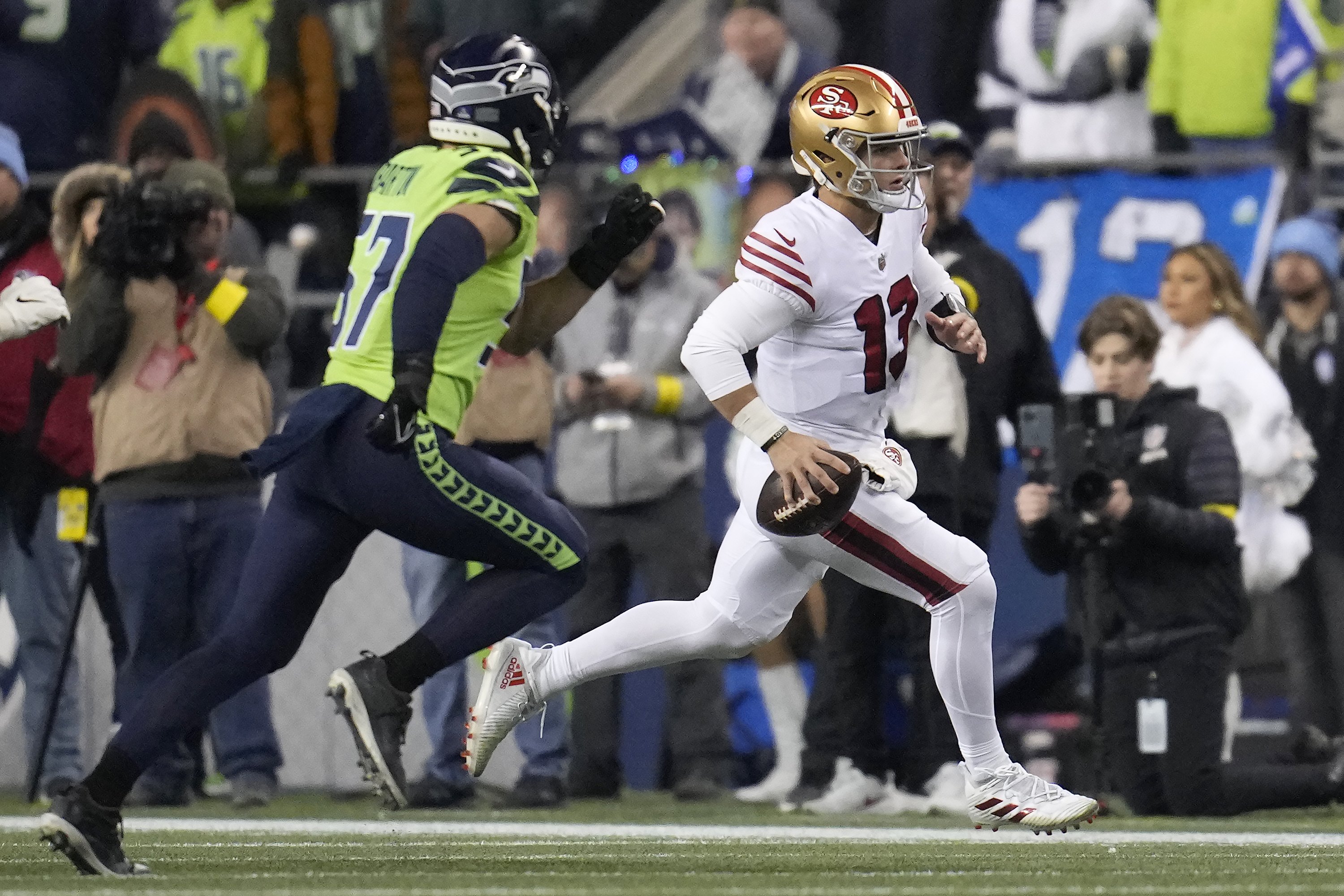 Brock Purdy (13), quarterback de 49ers de San Francisco, corre para tratar de eludir a Cody Barton (57), linebacker de Seahawks de Seattle, durante la primera mitad del juego de la NFL en Seattle, el jueves 15 de diciembre de 2022. (AP Foto/Marcio Jose Sanchez)