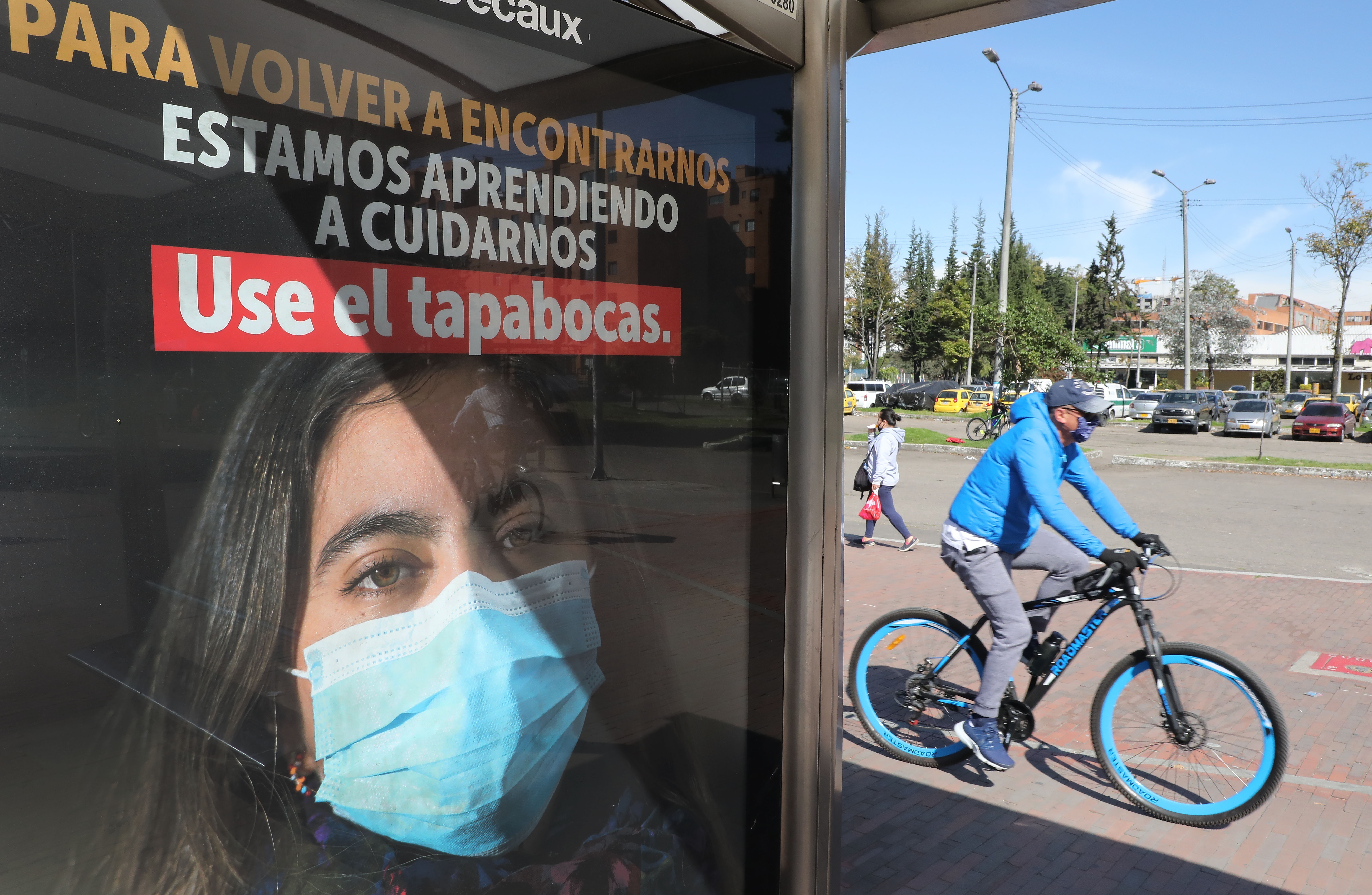 Un hombre circula en bicicleta junto a un anuncio que fomenta el uso del tapabocas, en Bogotá (Colombia). EFE/ Carlos Ortega/Archivo
