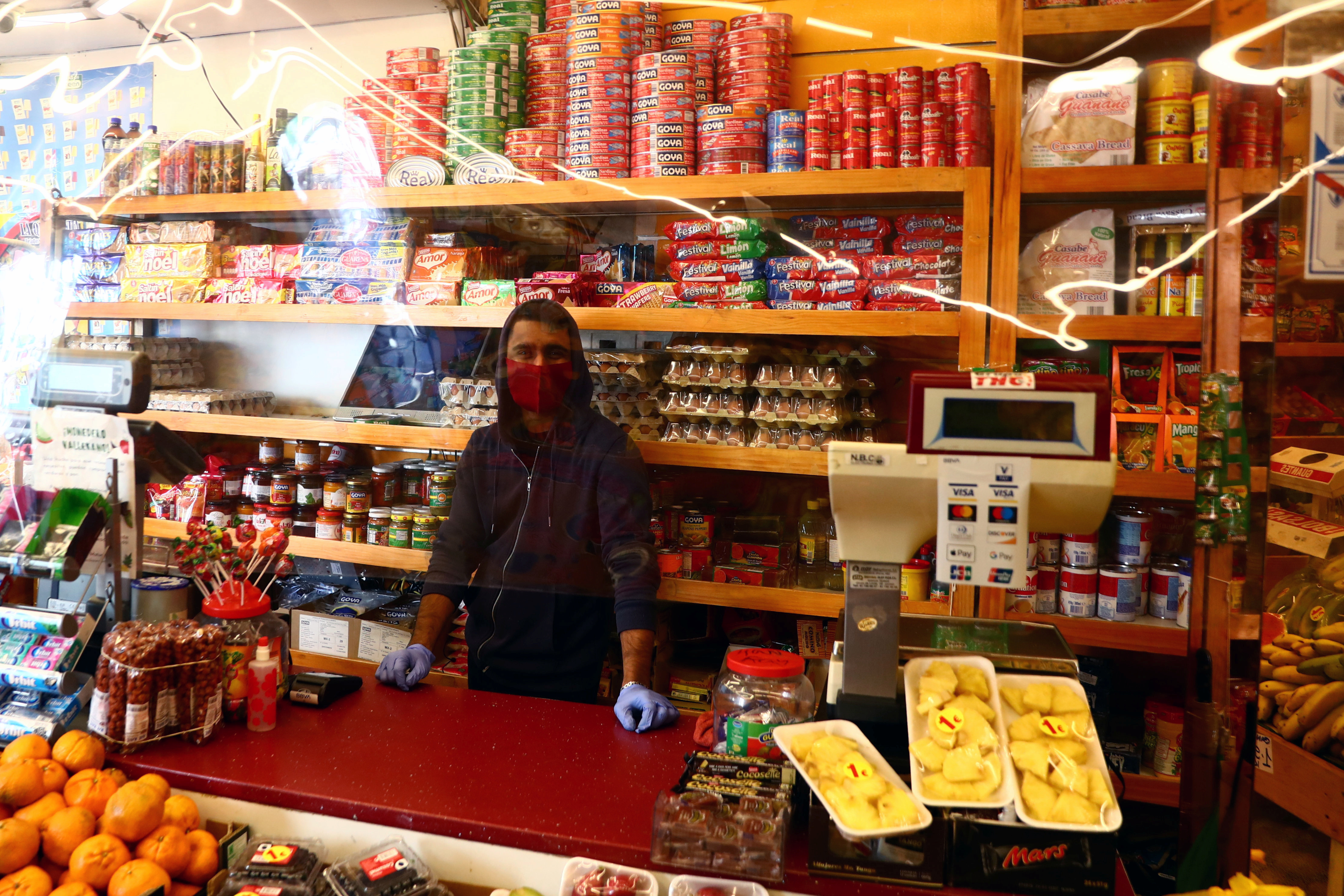 Un empleado con una máscara facial espera a los clientes detrás de una cortina de plástico en una tienda de alimentos en Madrid (REUTERS/Sergio Pérez)