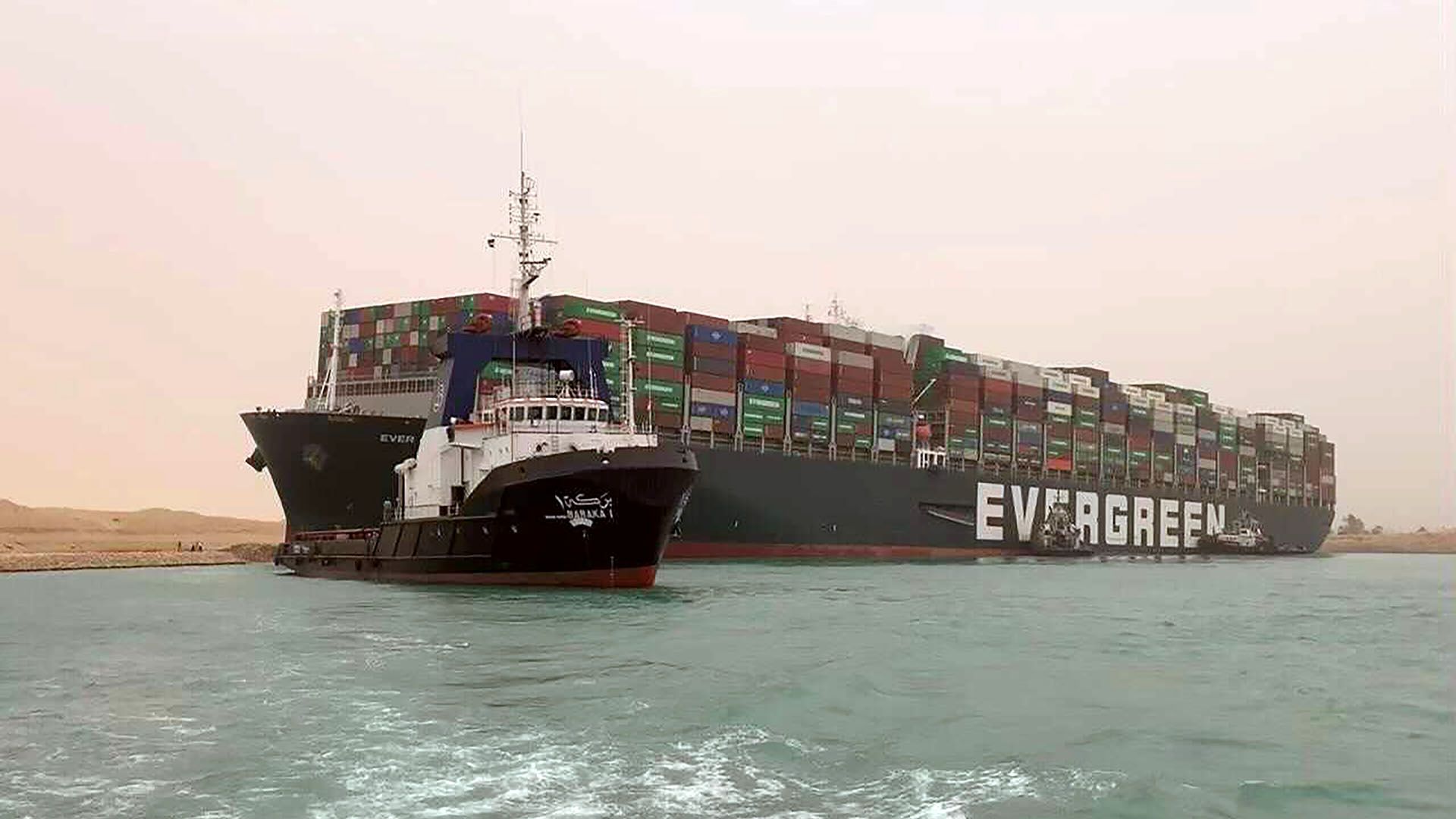 Un barco navega frente al enorme carguero MV Ever Green, luego de que giró de lado en el Canal de Suez de Egipto, bloqueando el tráfico en un vía navegable Este-Oeste crucial para el transporte marítimo mundial (Autoridad del Canal de Suez vía AP)