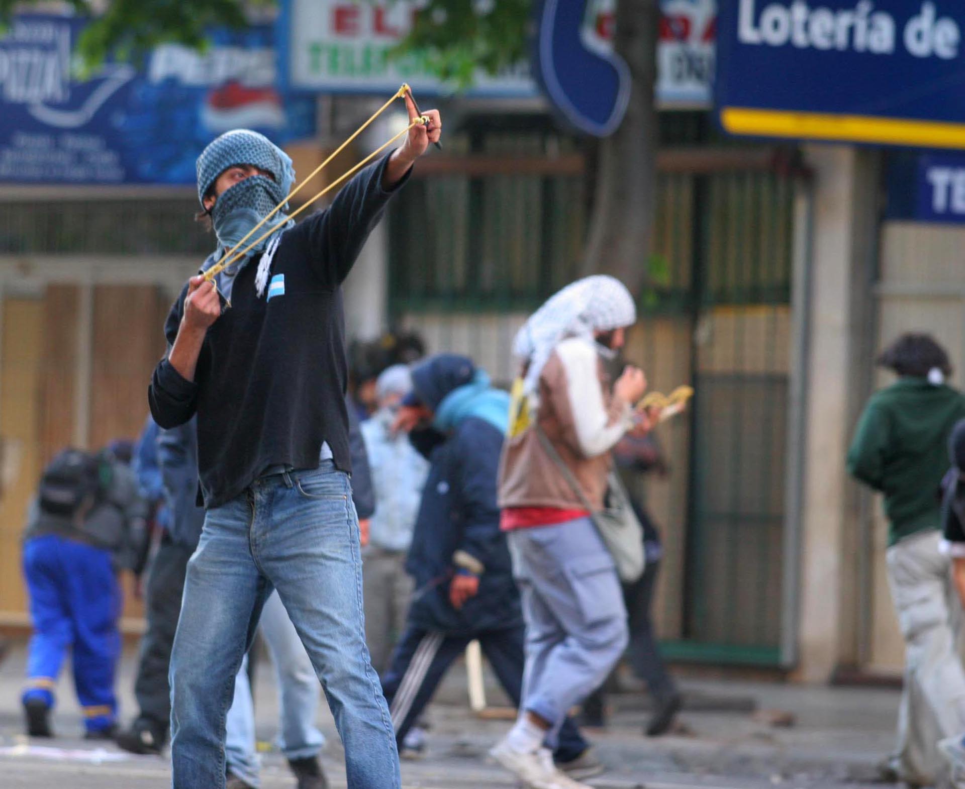Un manifestante arroja piedras con una gomera durante la marcha en rechazo a la visita del Presidente de EEUU