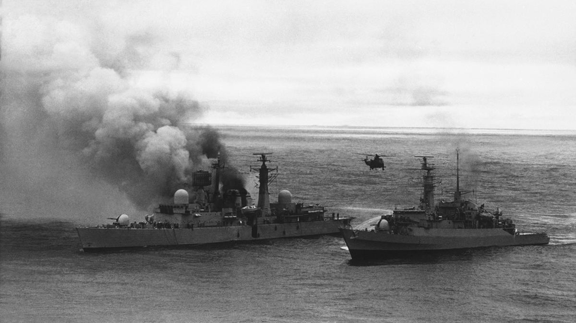 A frigate closes in on the damaged HMS Sheffield, spraying water from her hoses as a Sea King helicopter hovers over head in Falkland Islands, on May 28, 1982. Two Argentine Super Etendard strike fighters attacked the ship with missiles, starting fires that burned for days, before the Sheffield finally sank. Twenty lives were lost.  (AP)