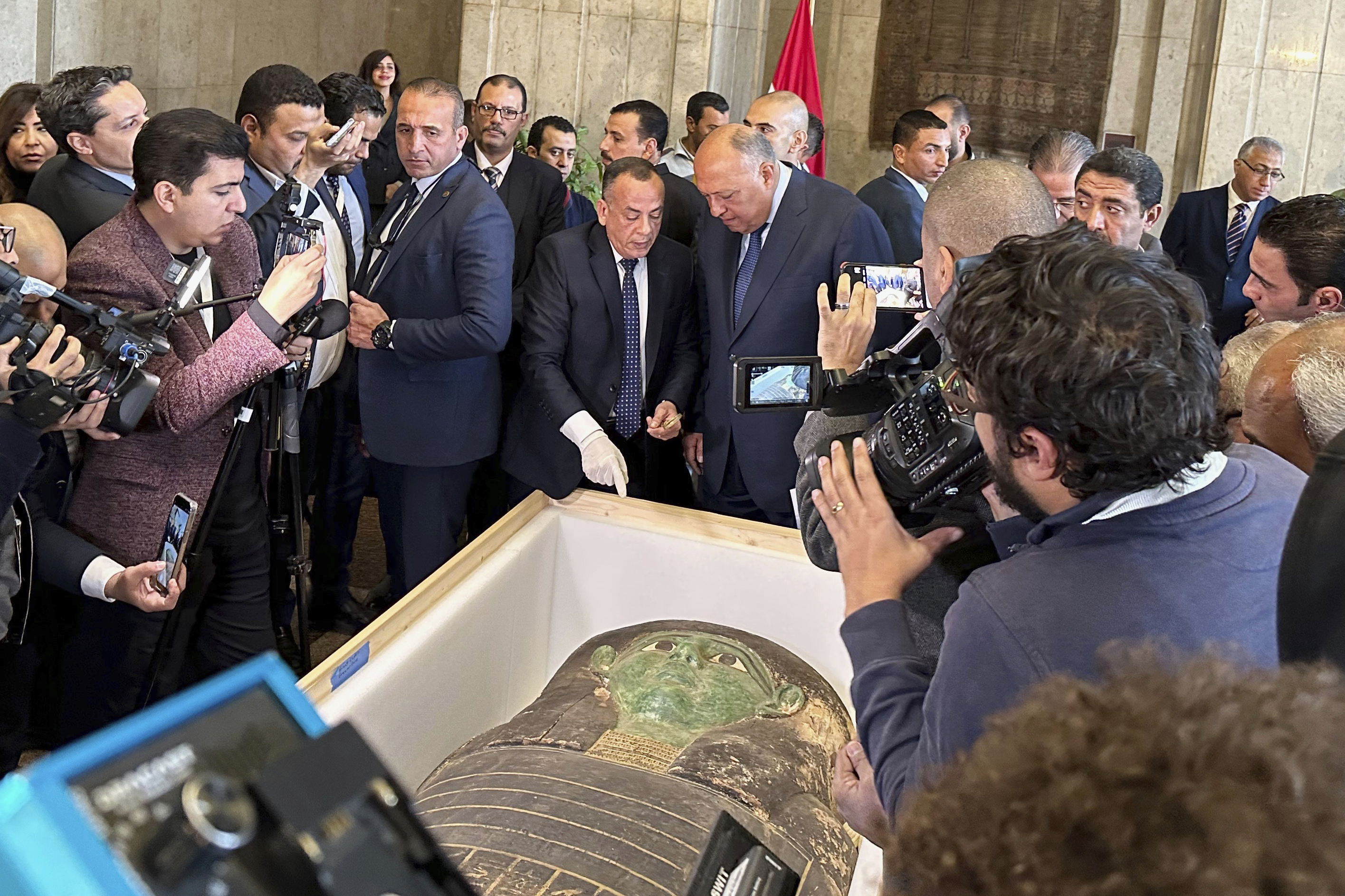 El ministro de Relaciones Exteriores, Sameh Shoukry, centro derecha, y Mostafa Waziri, alto funcionario del Consejo Supremo de Antigüedades, hablan frente a un antiguo sarcófago de madera durante una ceremonia de entrega en el Ministerio de Relaciones Exteriores en El Cairo, Egipto, el lunes 2 de enero de 2023. (Foto AP/Mohamed Salah)

