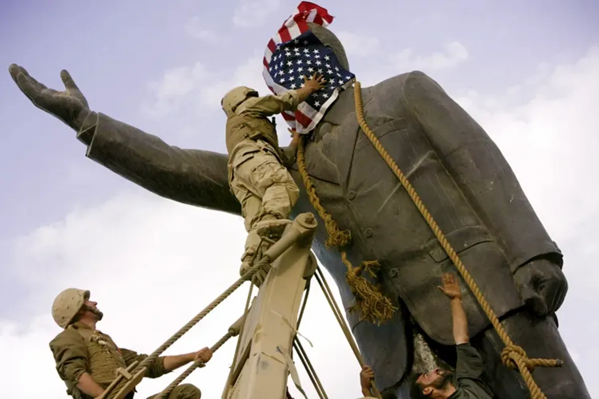 El cabo Edward Chin colocando la bandera estadounidense sobre la cara de la estatua de Saddam. Un minuto y medio más tarde la cambió por una bandera iraquí.