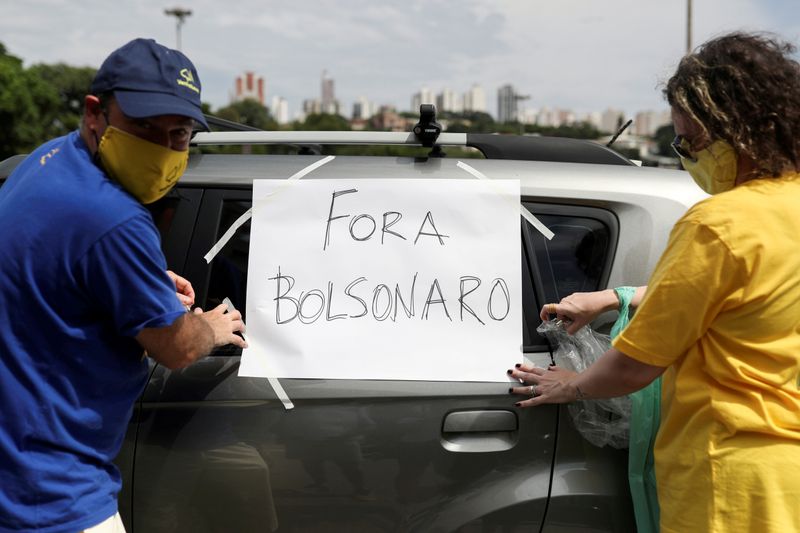 Dos manifestantes pega a su auto un cartel que dice "¡Fuera Bolsonaro!" en una manifestación contra el presidente en Sao Paulo. REUTERS/Amanda Perobelli