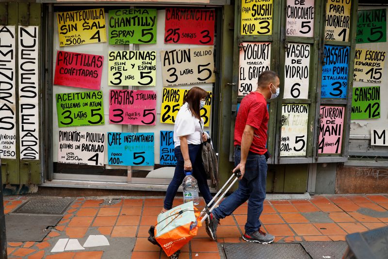 Personas pasan frente a una tienda de comestibles con carteles que anuncian los precios de los alimentos, en Caracas (REUTERS/Leonardo Fernández Viloria/Archivo)
