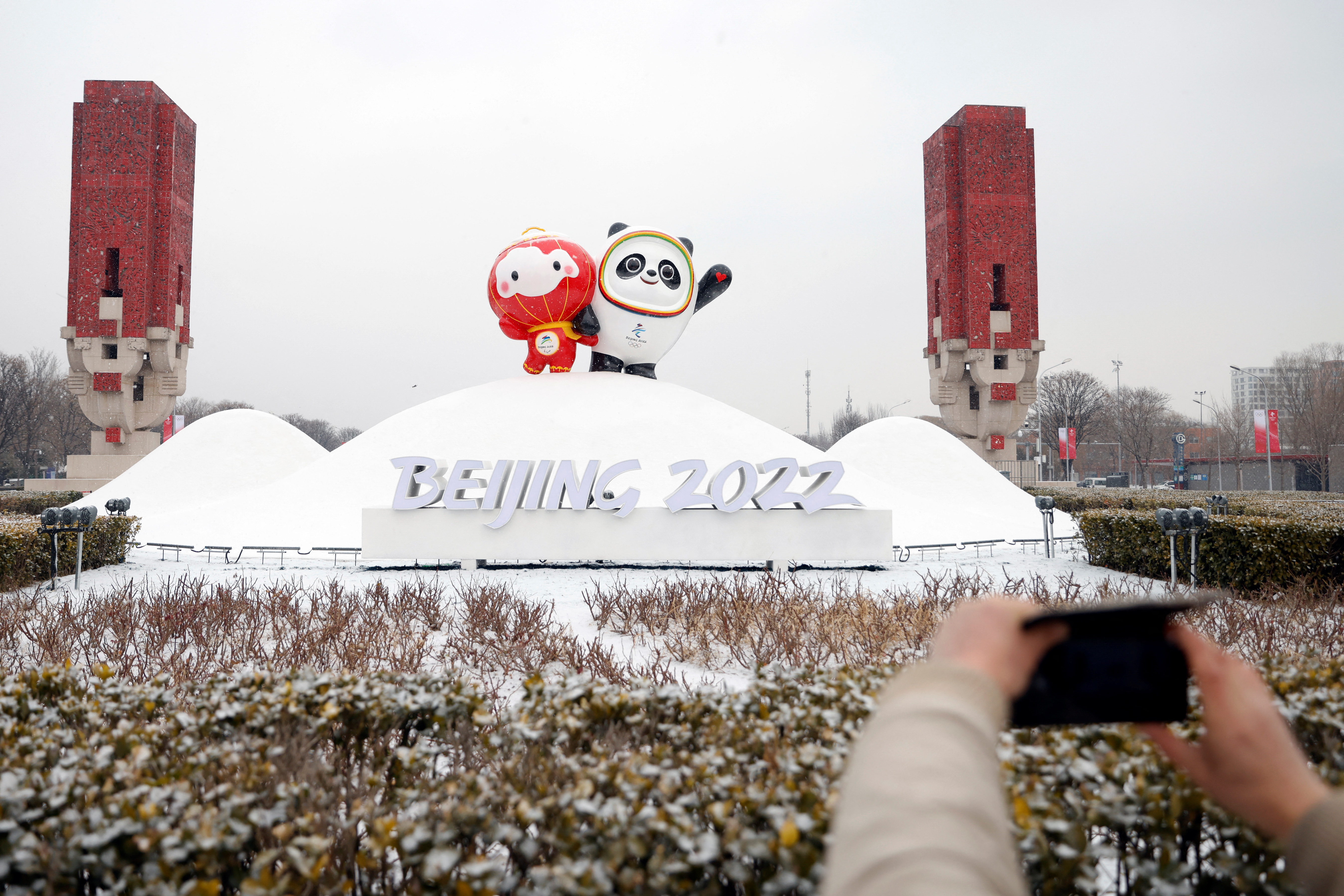 A pedestrian takes pictures of an installation featuring Bing Dwen Dwen and Shuey Rhon Rhon, mascots of the Beijing 2022 Winter Olympics and Paralympics, amid snowfall in Beijing, China January 20, 2022. REUTERS/Carlos Garcia Rawlins